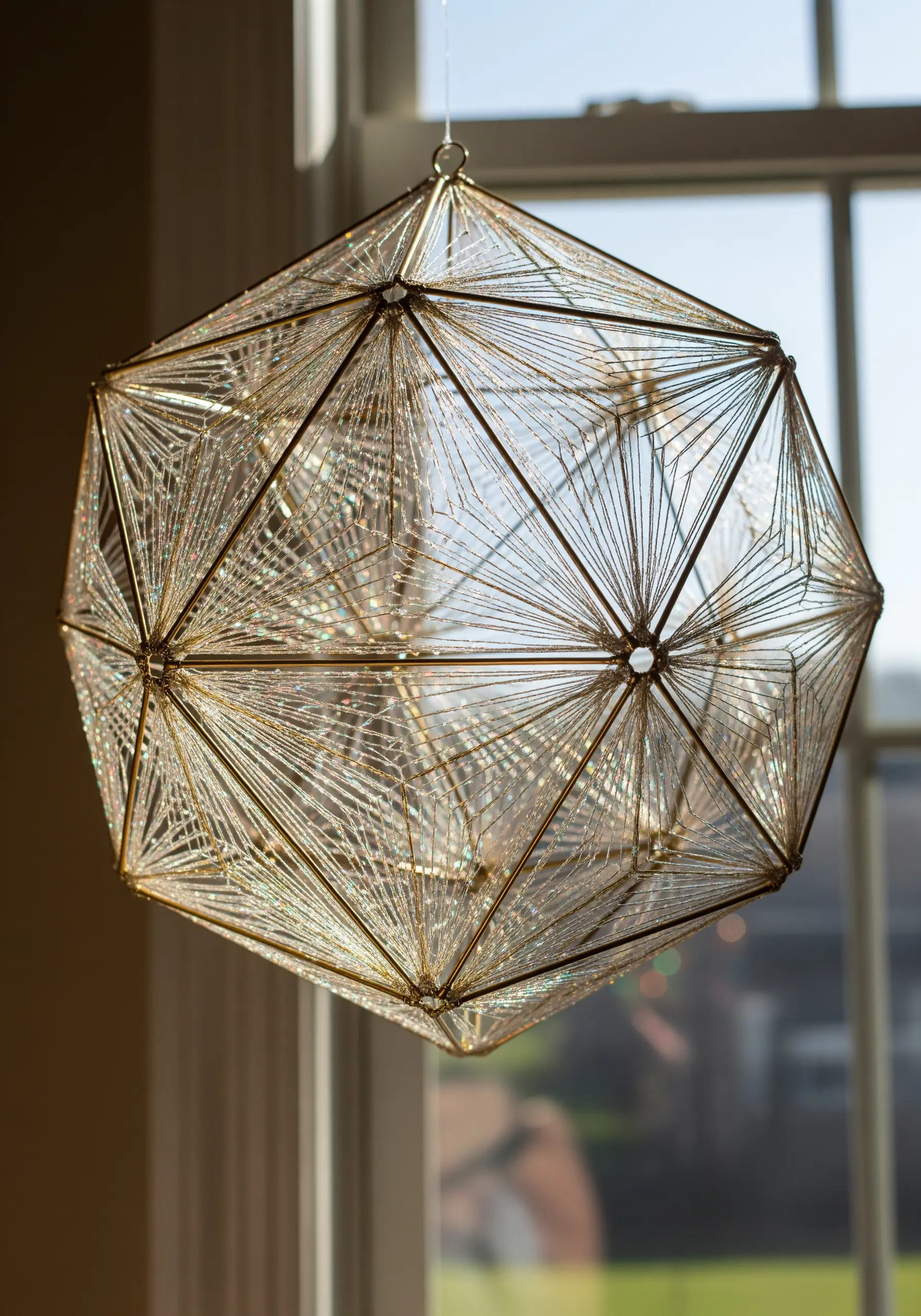 A complex geometric polyhedron made of gold wire, intricately wrapped with translucent glitter thread.