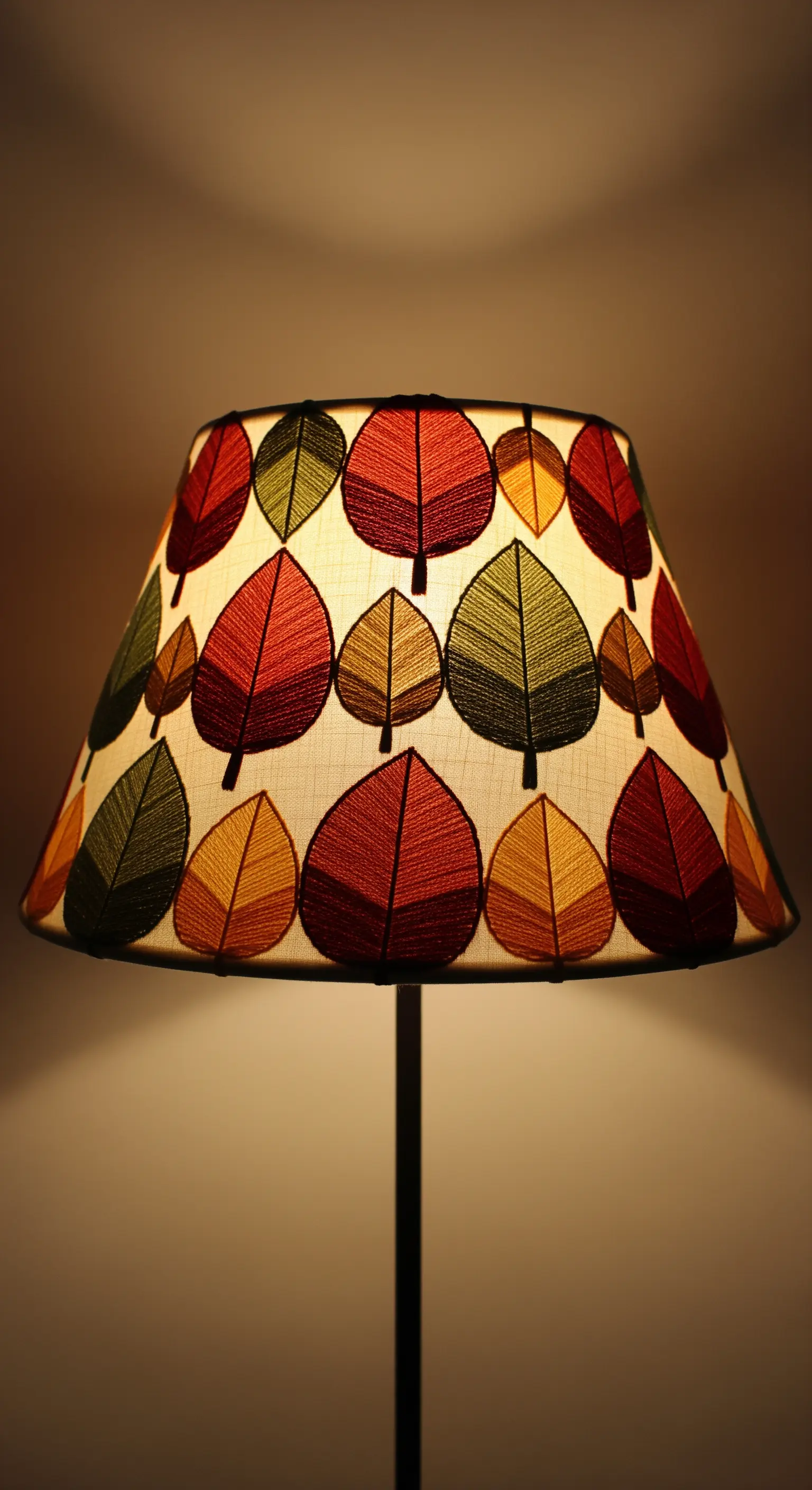 An embroidered lampshade with autumn leaves in gradient colors, glowing warmly.