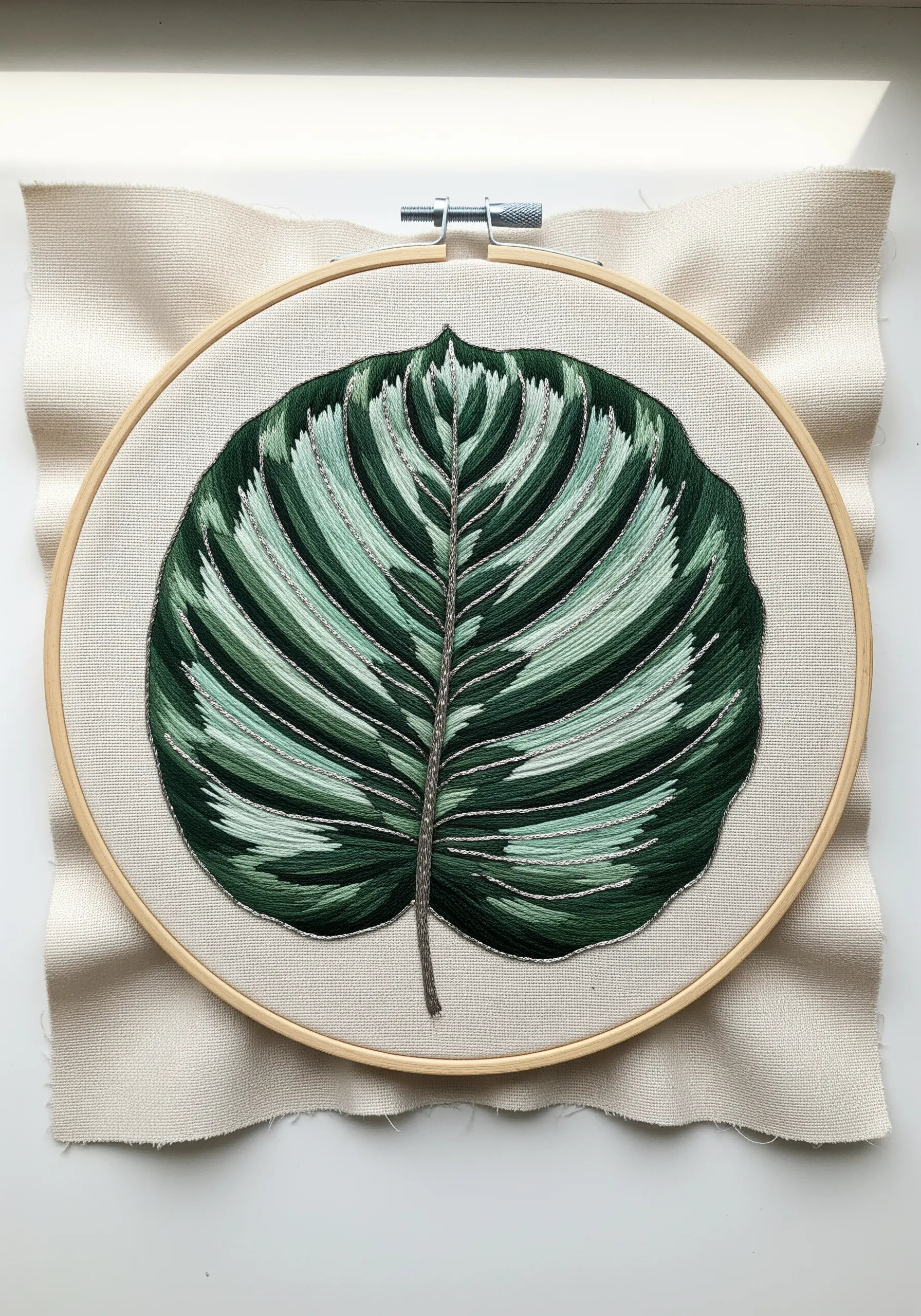Embroidered Calathea leaf in a hoop with green gradients and silver metallic veins.