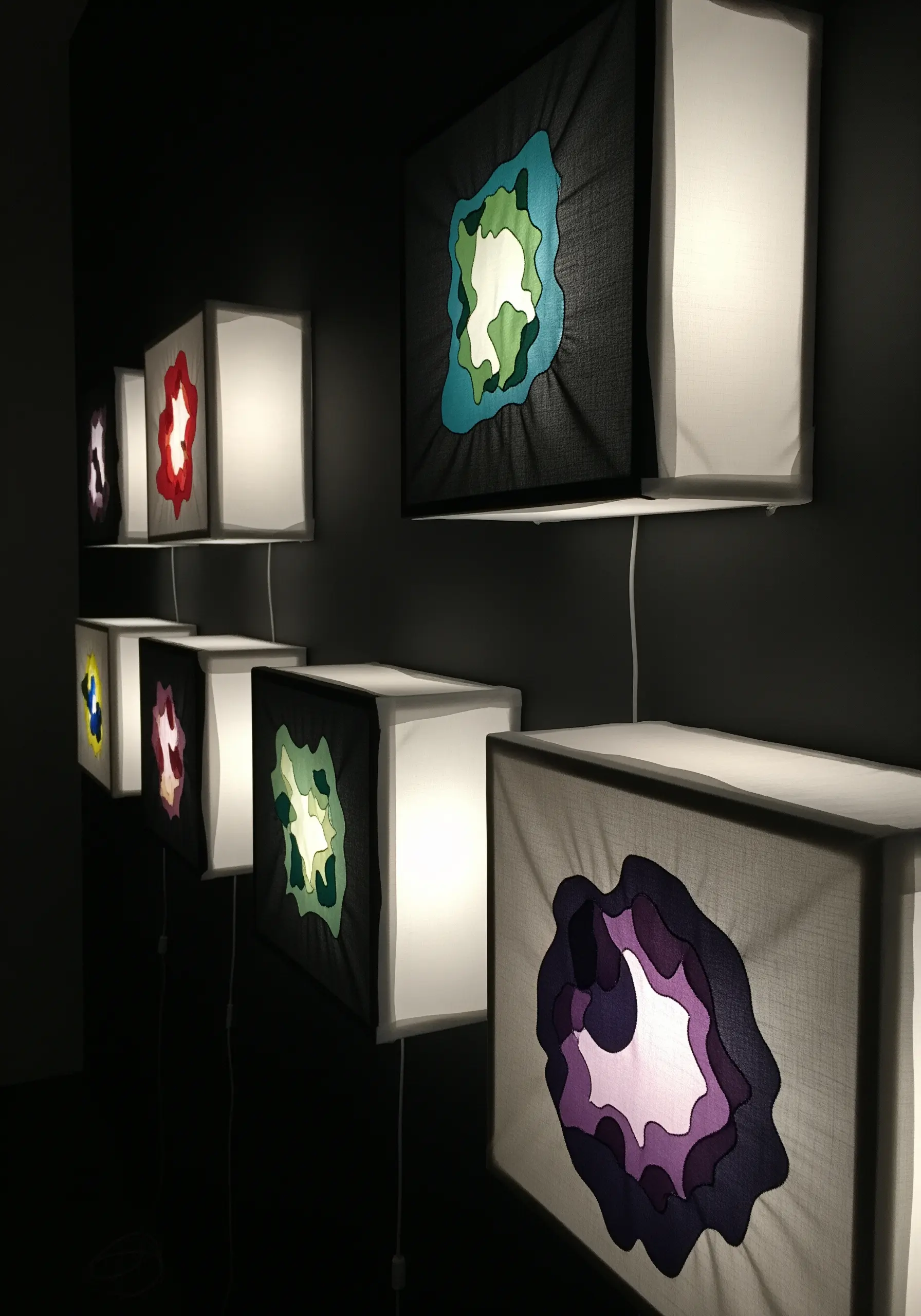 A row of lightboxes with layered, cut fabric in organic shapes creating a colorful glow.