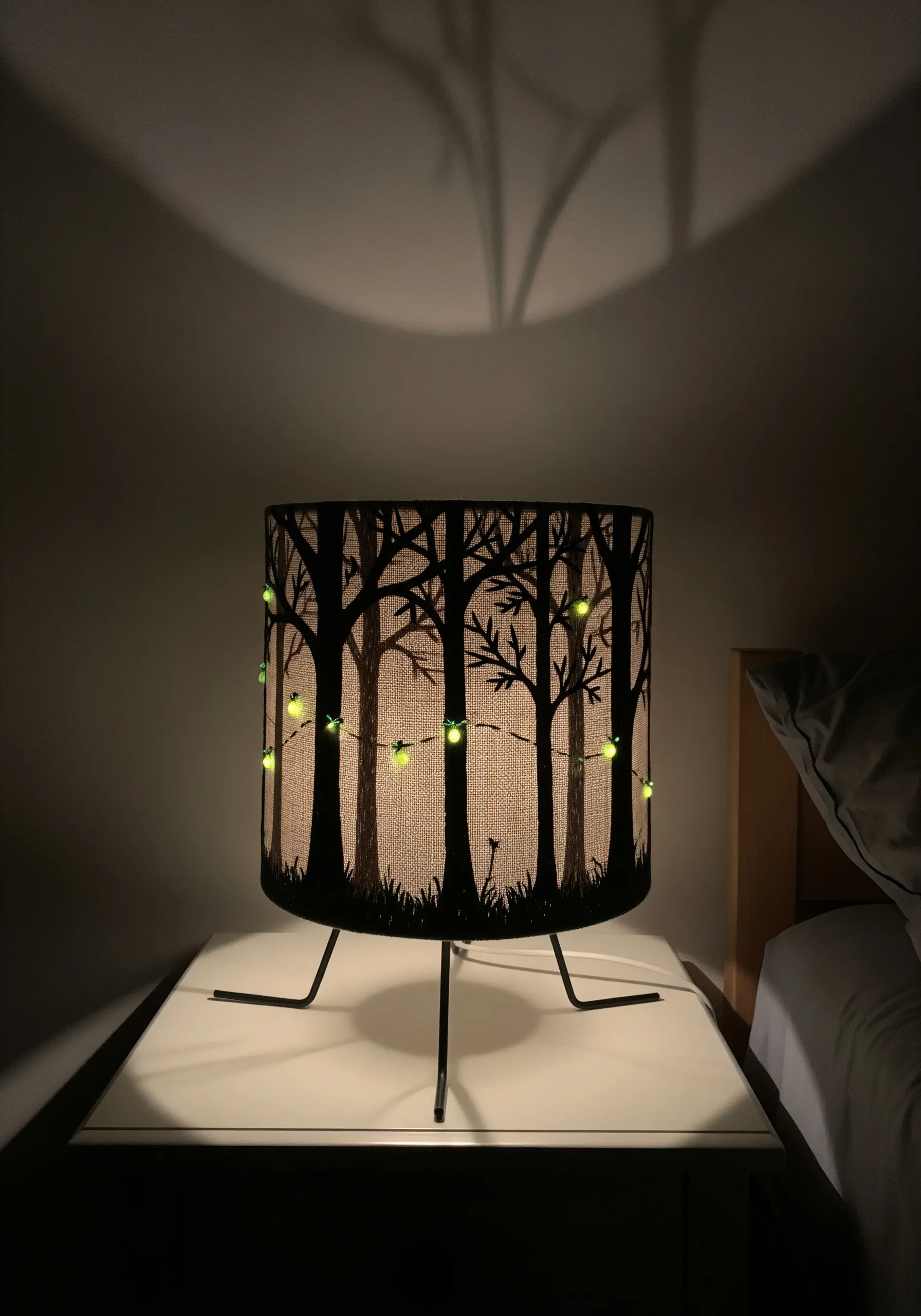 A lampshade with a black embroidered forest silhouette and glowing green fairy lights.
