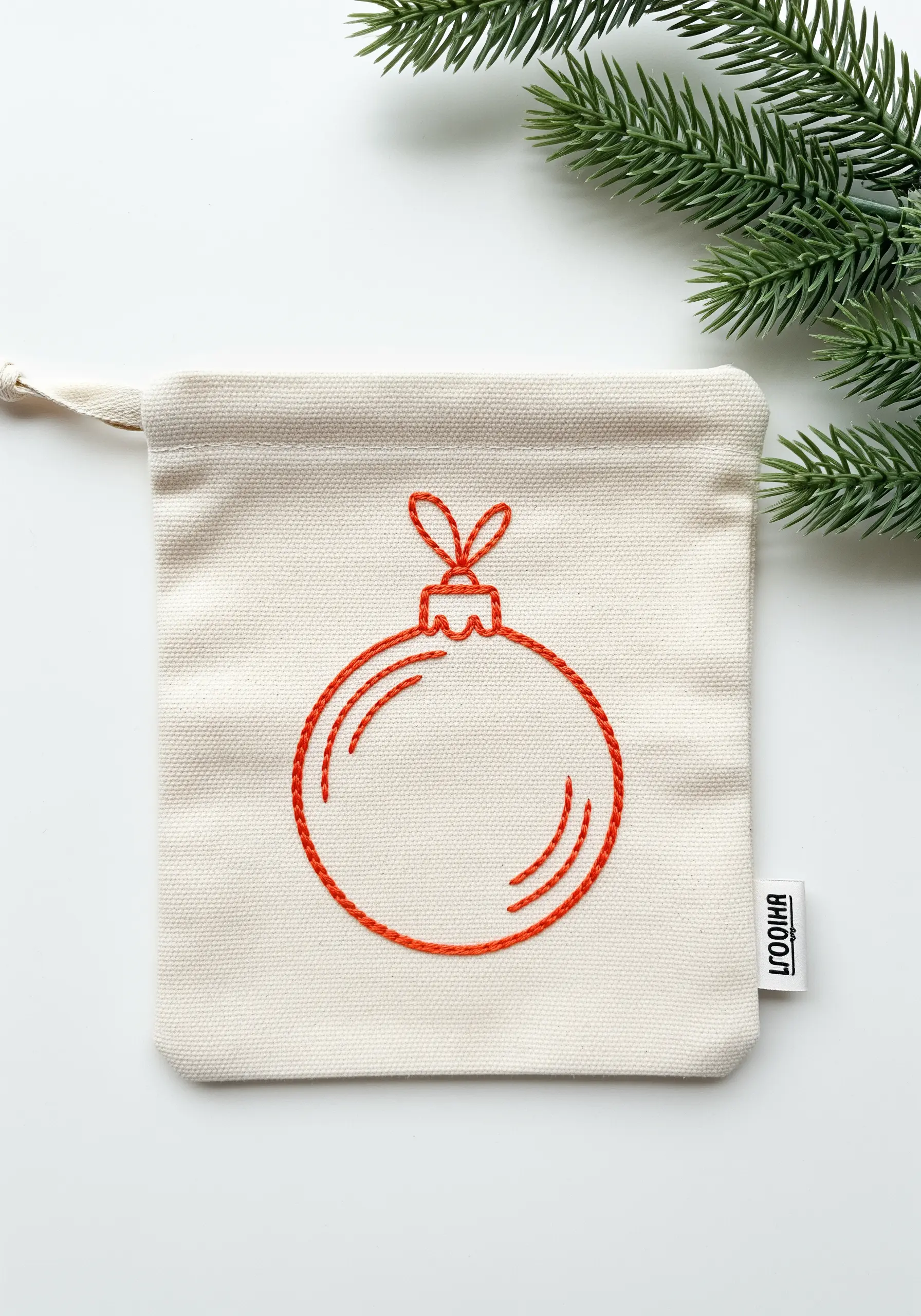 Red line art of a Christmas bauble embroidered on a small canvas drawstring bag.