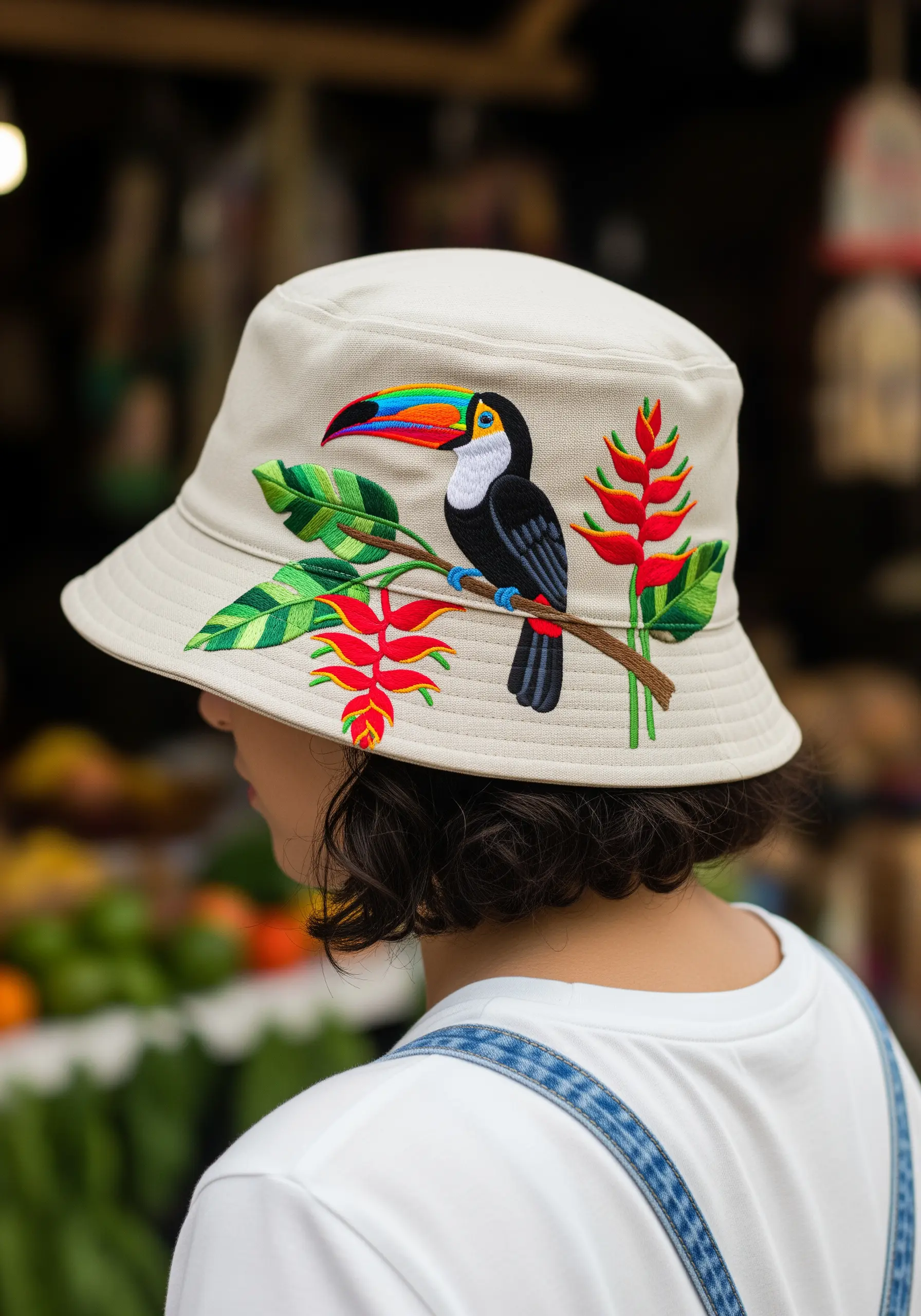 A colorful embroidered toucan perched on a branch with red heliconia flowers on a bucket hat.