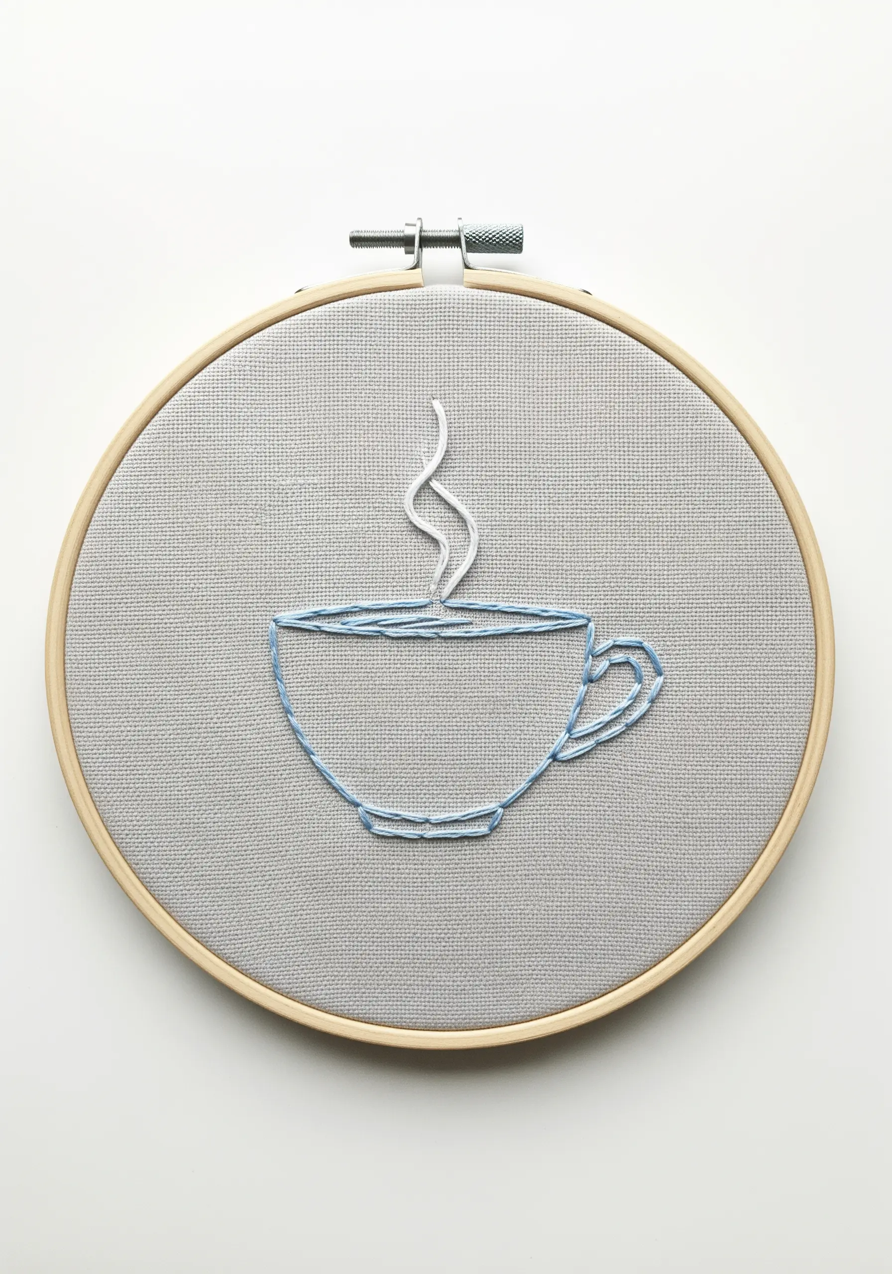A minimal line art embroidery of a coffee cup with steam, stitched in blue and white thread.