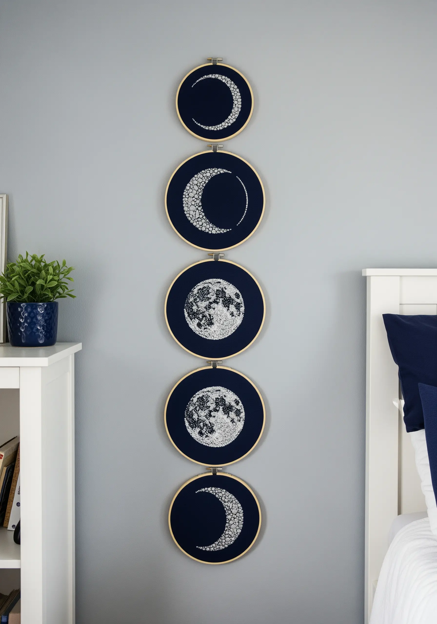 A vertical display of five embroidery hoops showing the phases of the moon in silver thread.