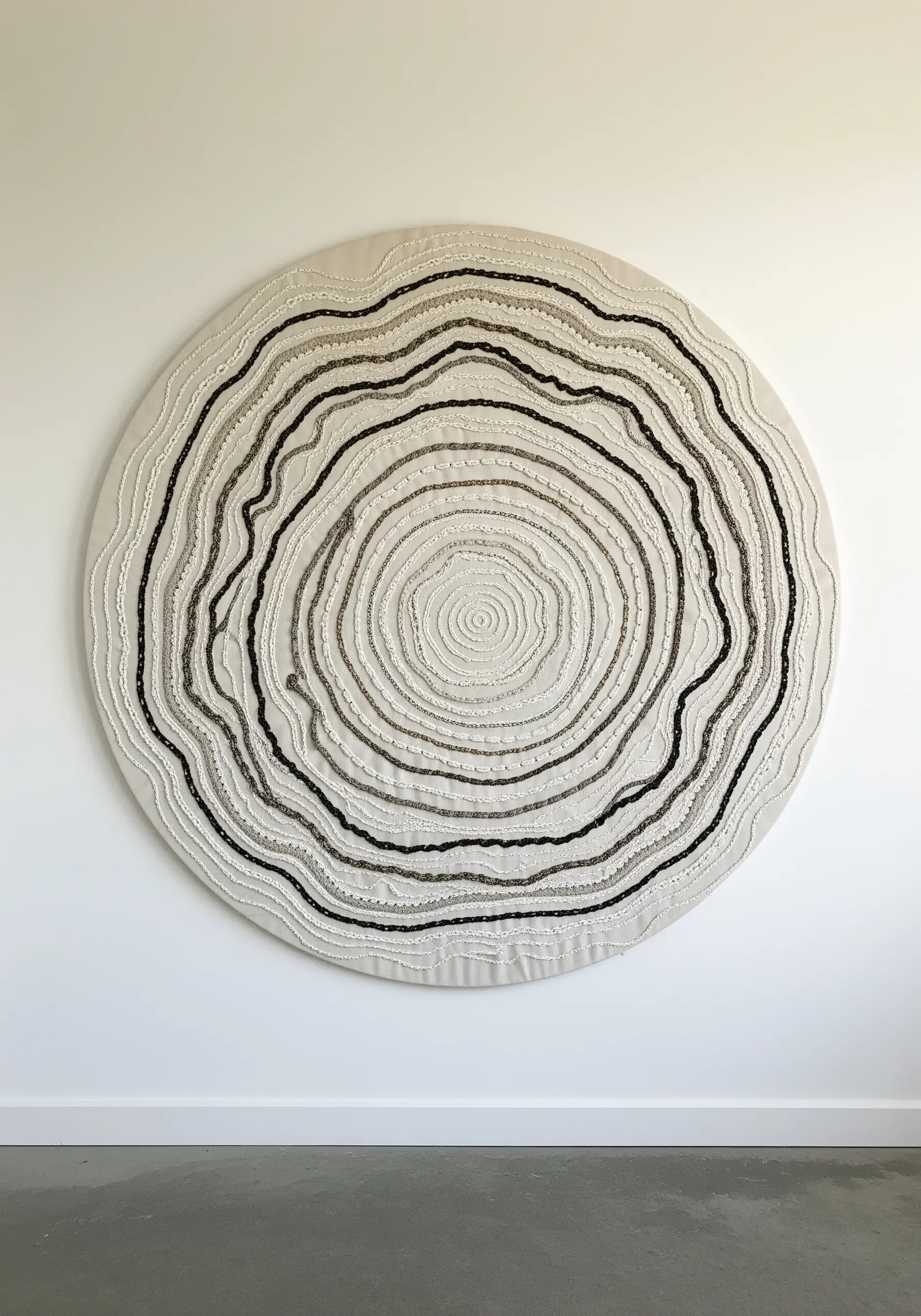 Large circular wall art with concentric rings of raised stitches mimicking tree rings.