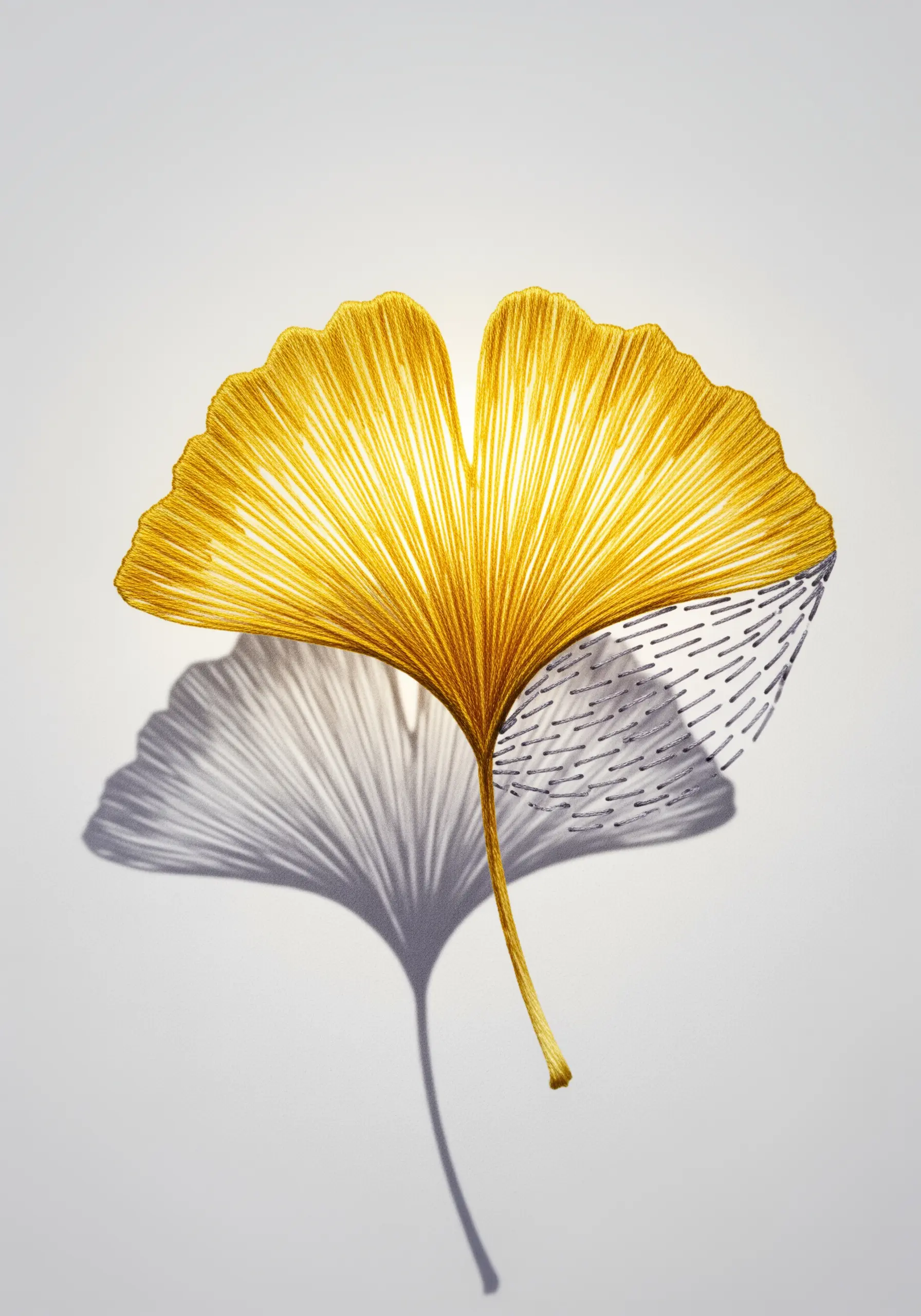 Golden ginkgo leaf embroidery with a graphic, open-stitch shadow in silver thread.