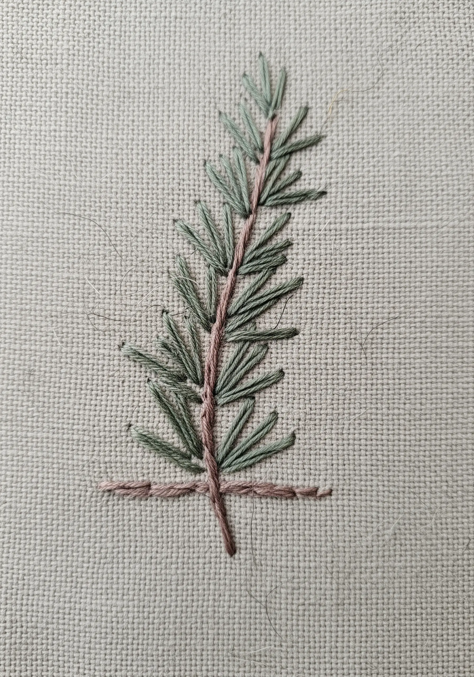 Minimalist embroidered pine sprig with light green needles and a dusty pink stem.