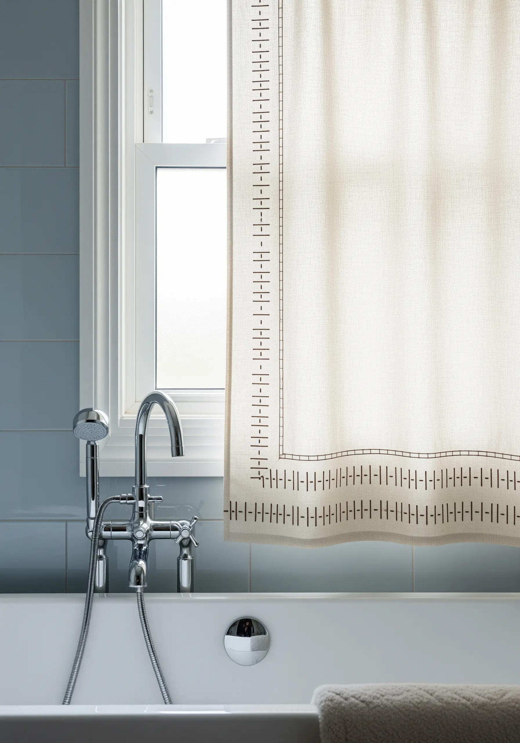 A minimalist border of varied vertical and horizontal stitches on a shower curtain.