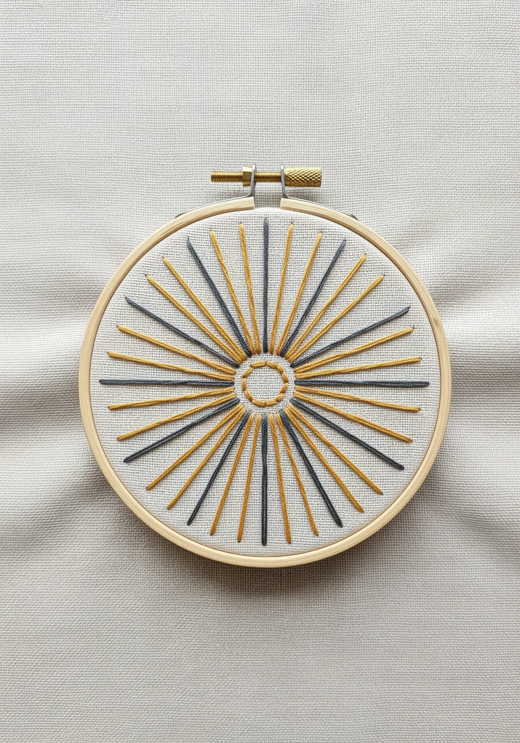 A geometric sunburst motif with alternating gold and charcoal straight stitches.