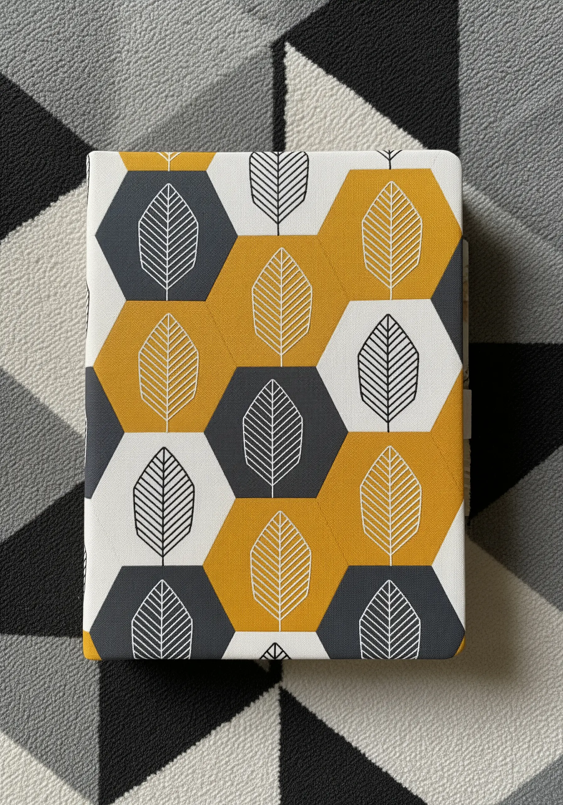 Simple outlined leaves embroidered inside a geometric pattern of yellow, grey, and white hexagons.