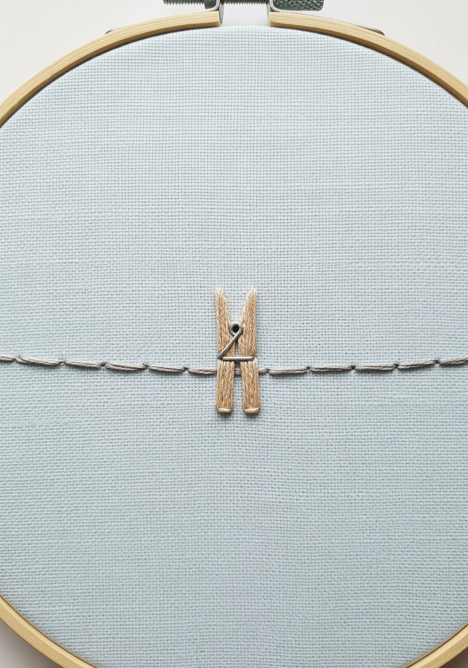 A real clothespin attached to fabric, with an embroidered clothesline running through it.
