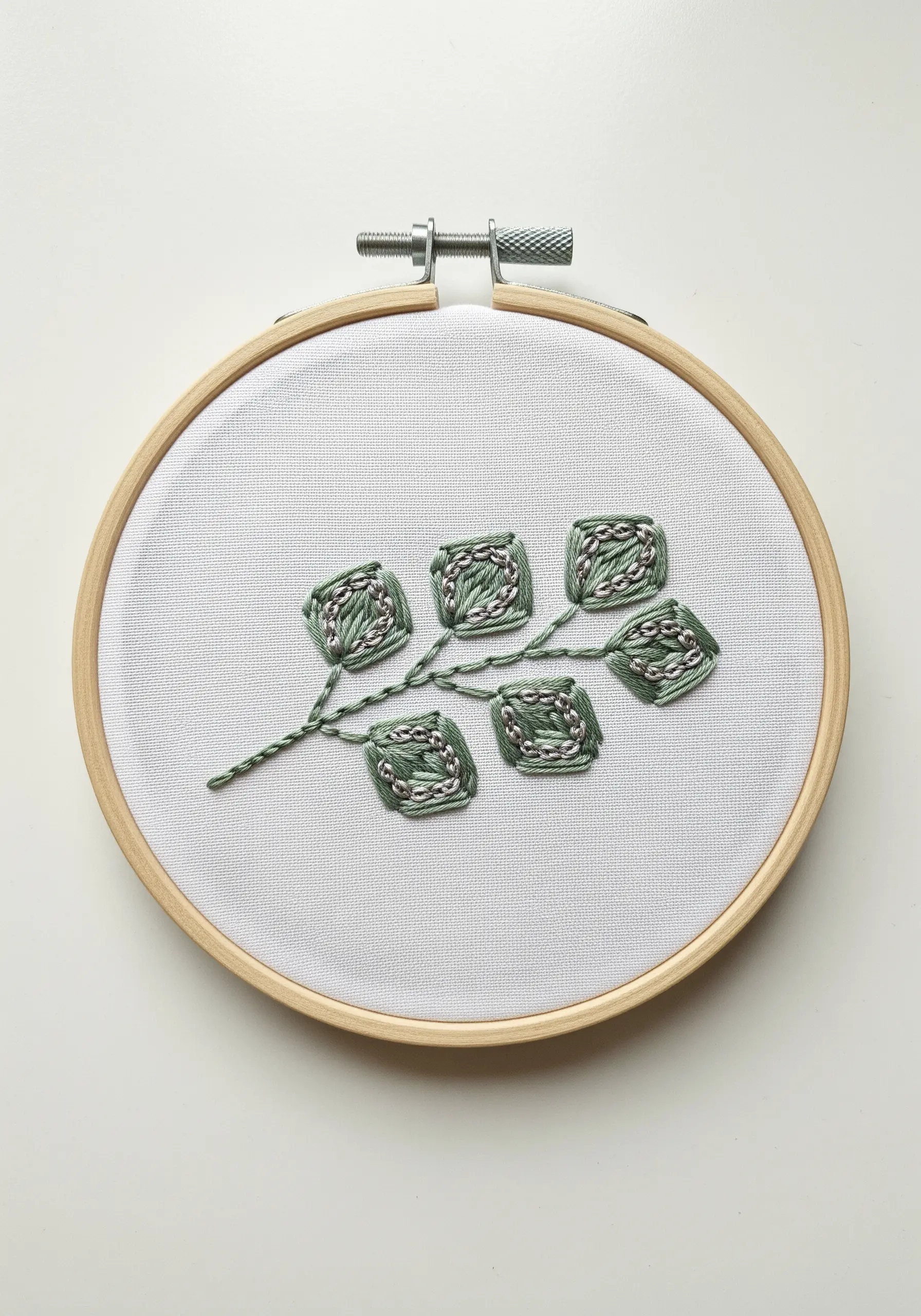 Embroidered botanical branch with green outlines and silver seed bead filling for leaves.