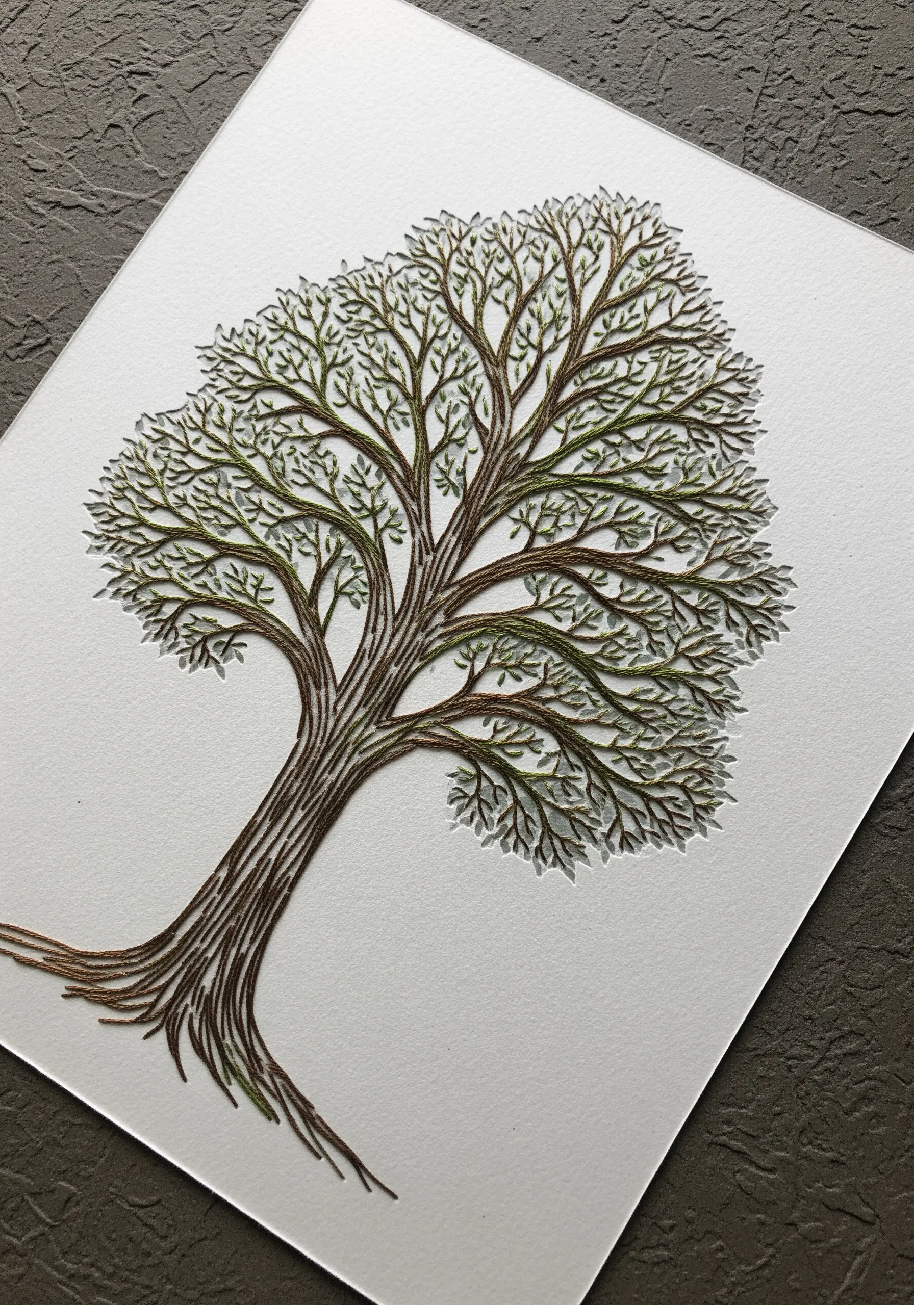 An intricate paper-cut tree with tiny green and brown stitches for leaves.
