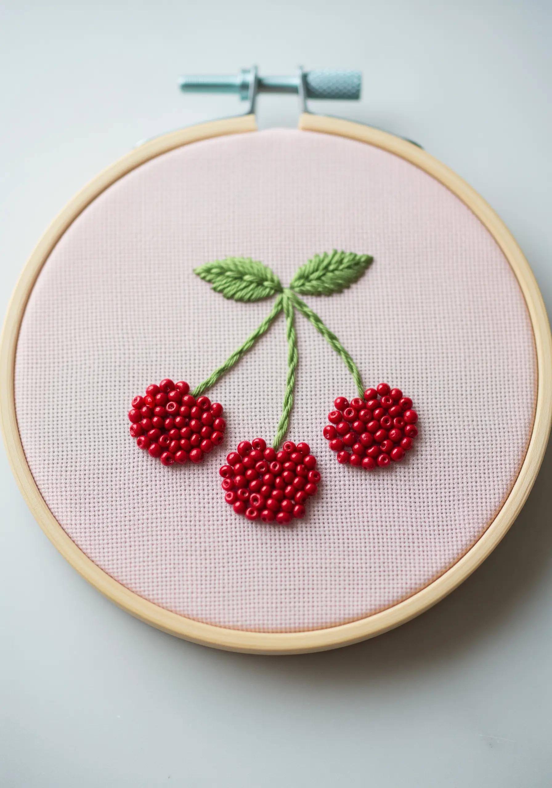 Three cherries with leaves; the cherries are made of red seed beads.