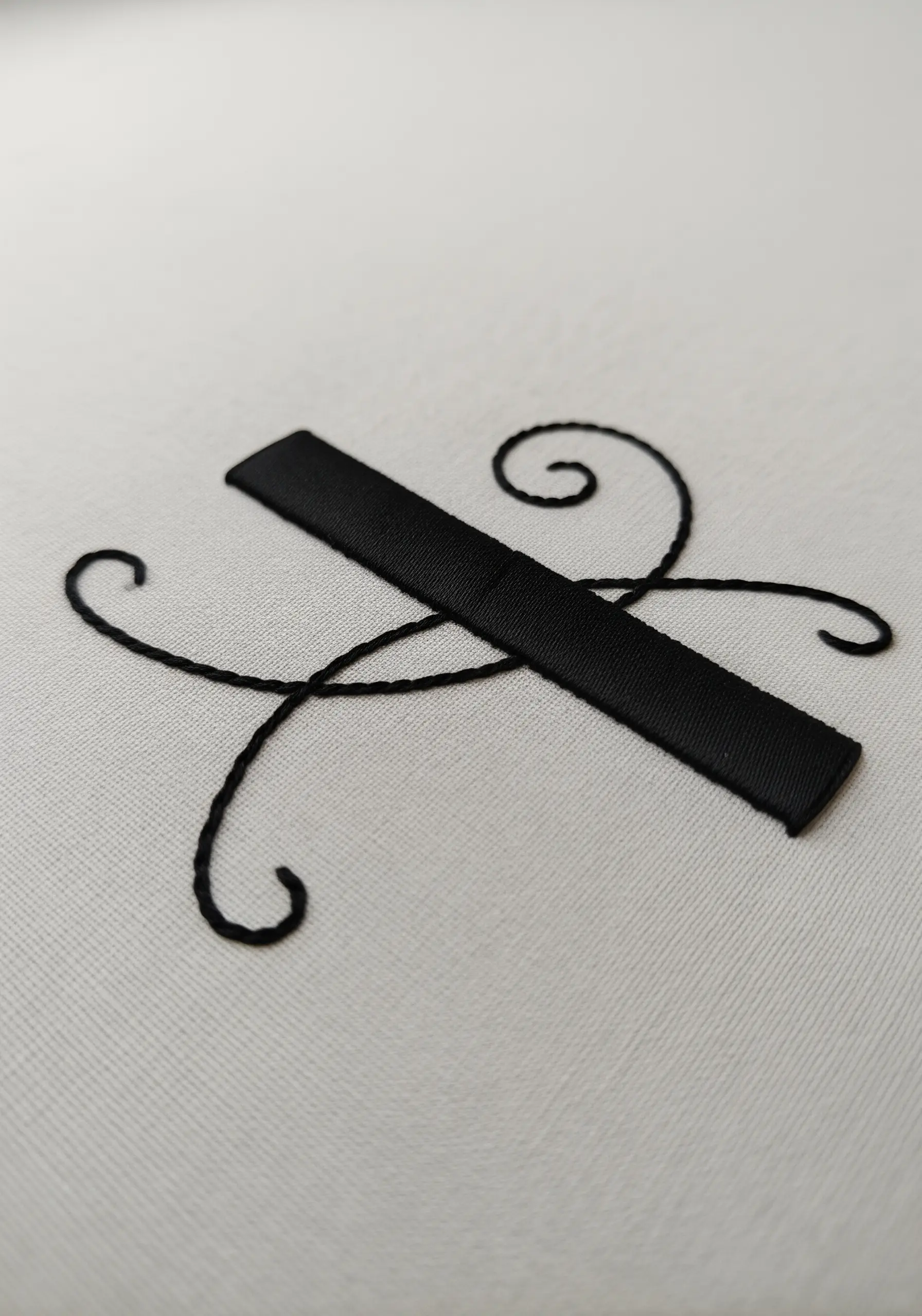 A combination of a flat black satin ribbon and fine black thread swirls on white fabric.
