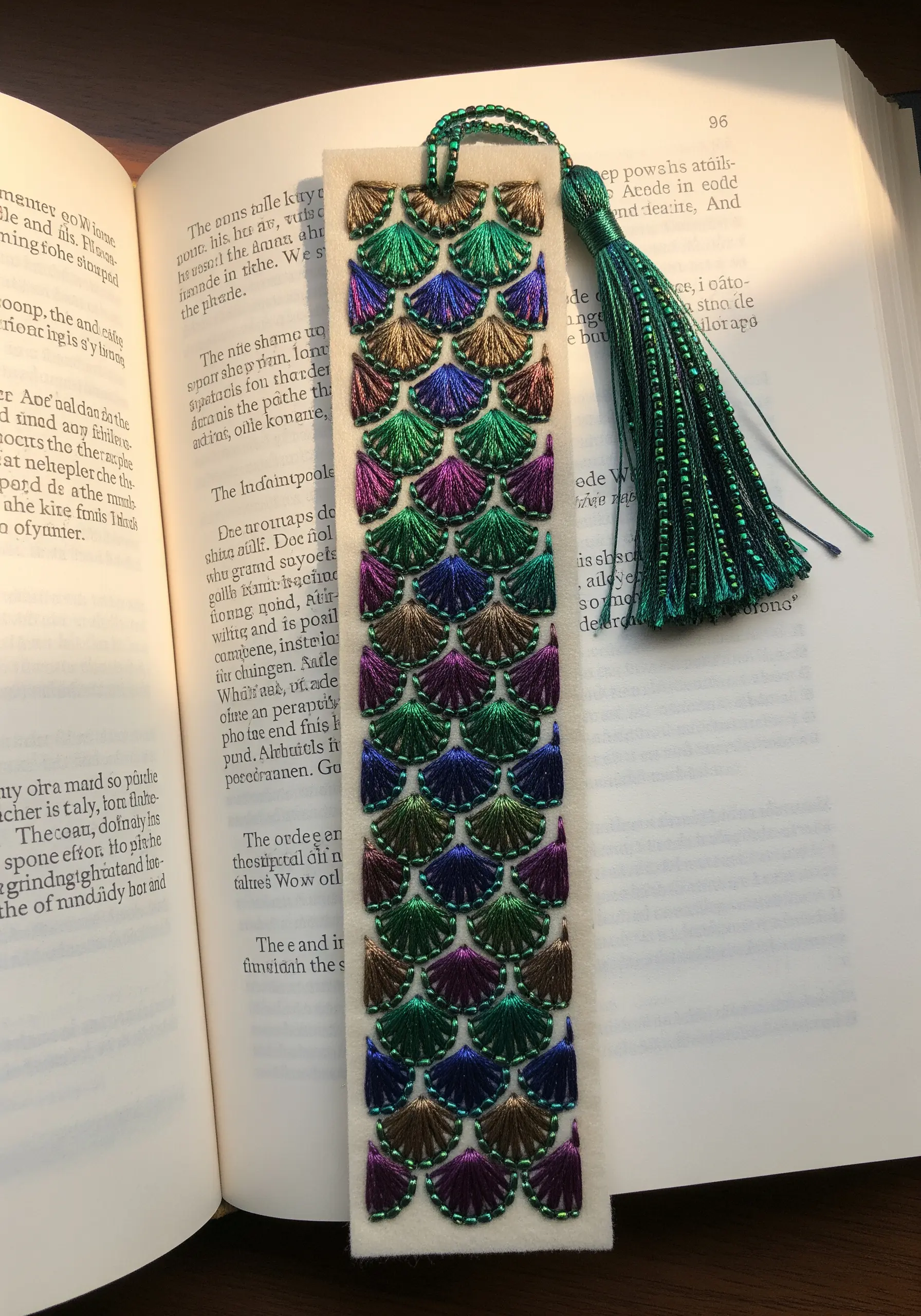 A bookmark with an intricate mermaid scale pattern embroidered in jewel-toned variegated thread.