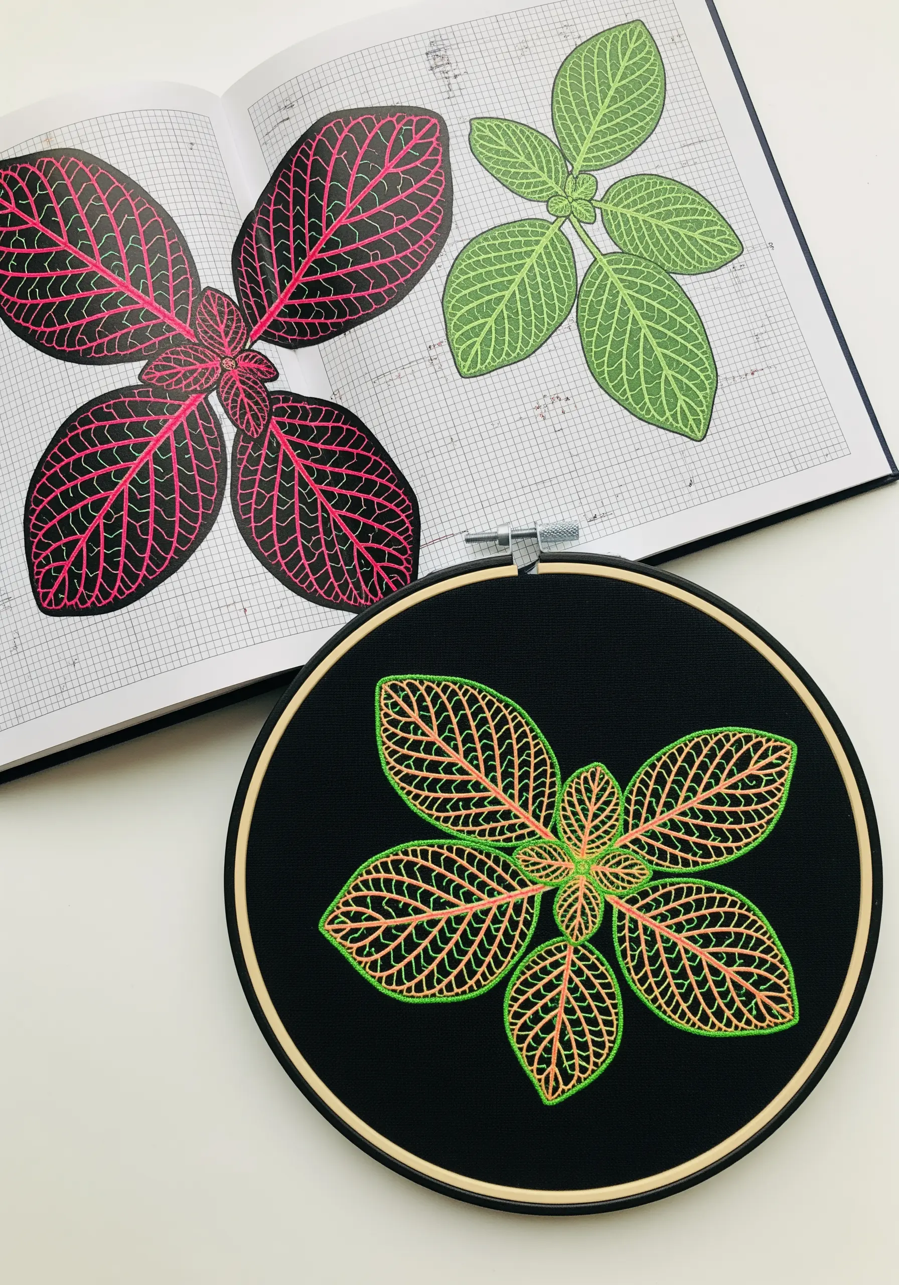 Line art embroidery of a nerve plant with neon veins on black fabric in a hoop.