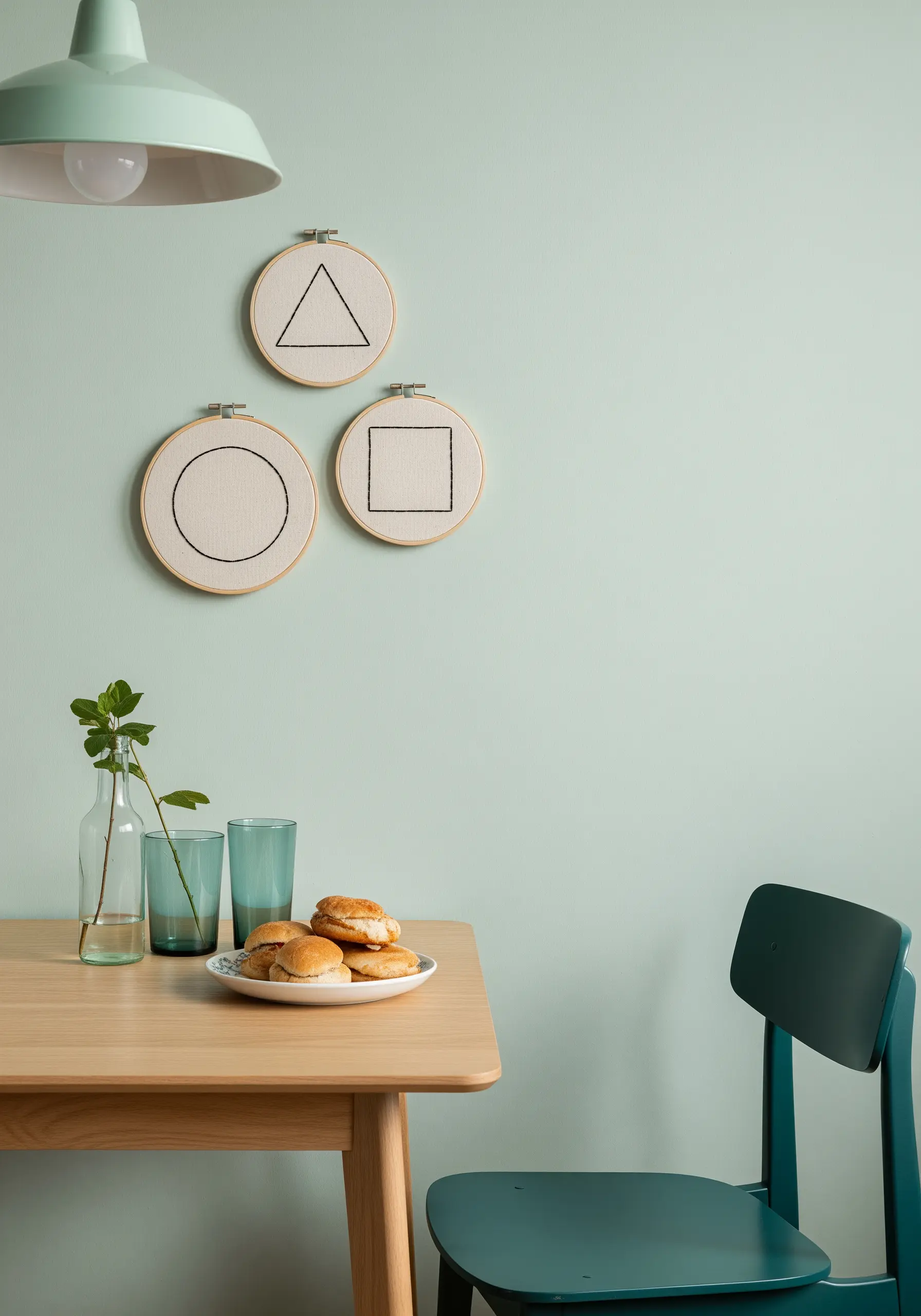 Three small embroidery hoops, each with a single black geometric shape: a circle, triangle, and square.