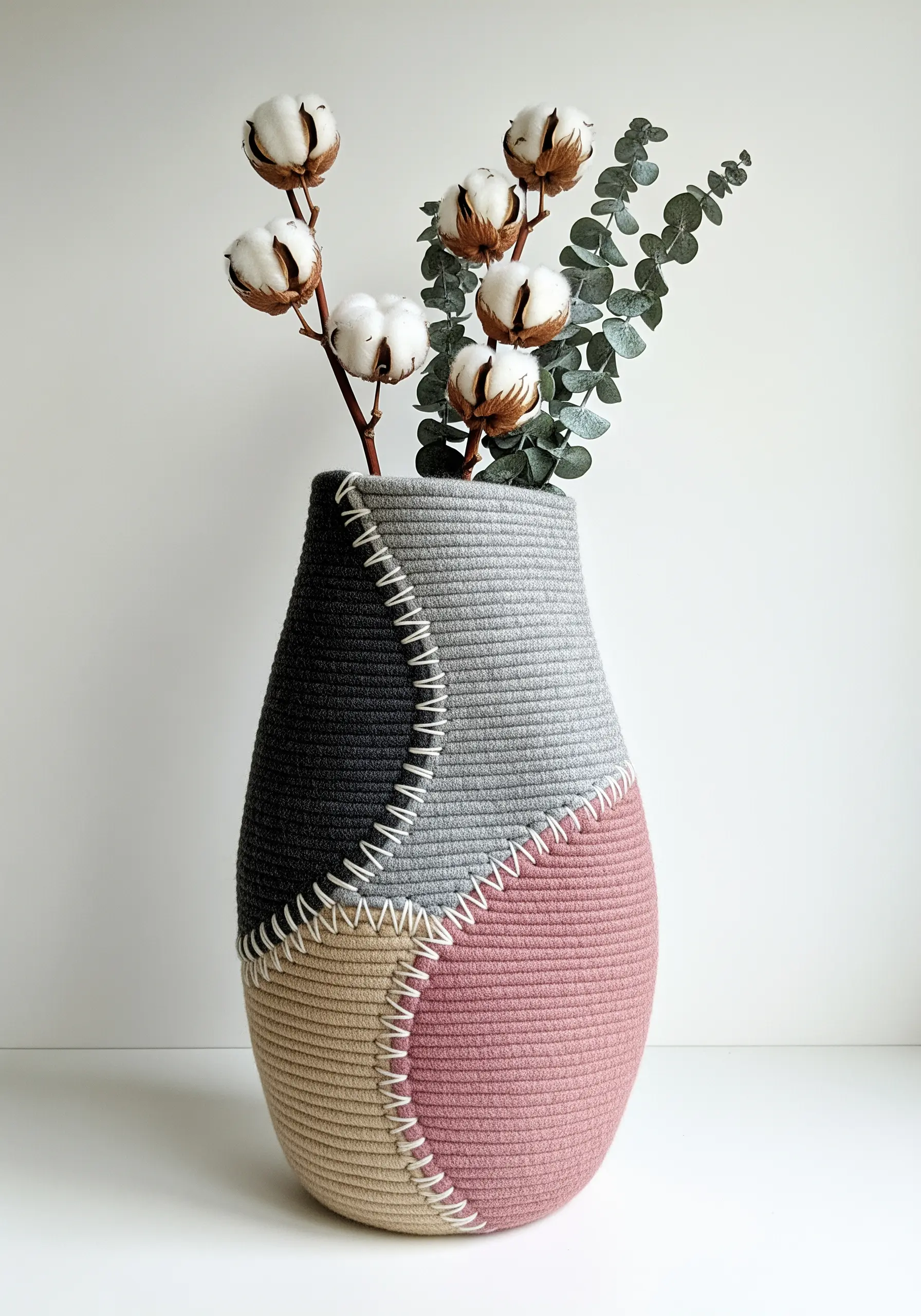 A color-blocked coiled rope vase in grey, pink, and black, joined with a bold white whipstitch.