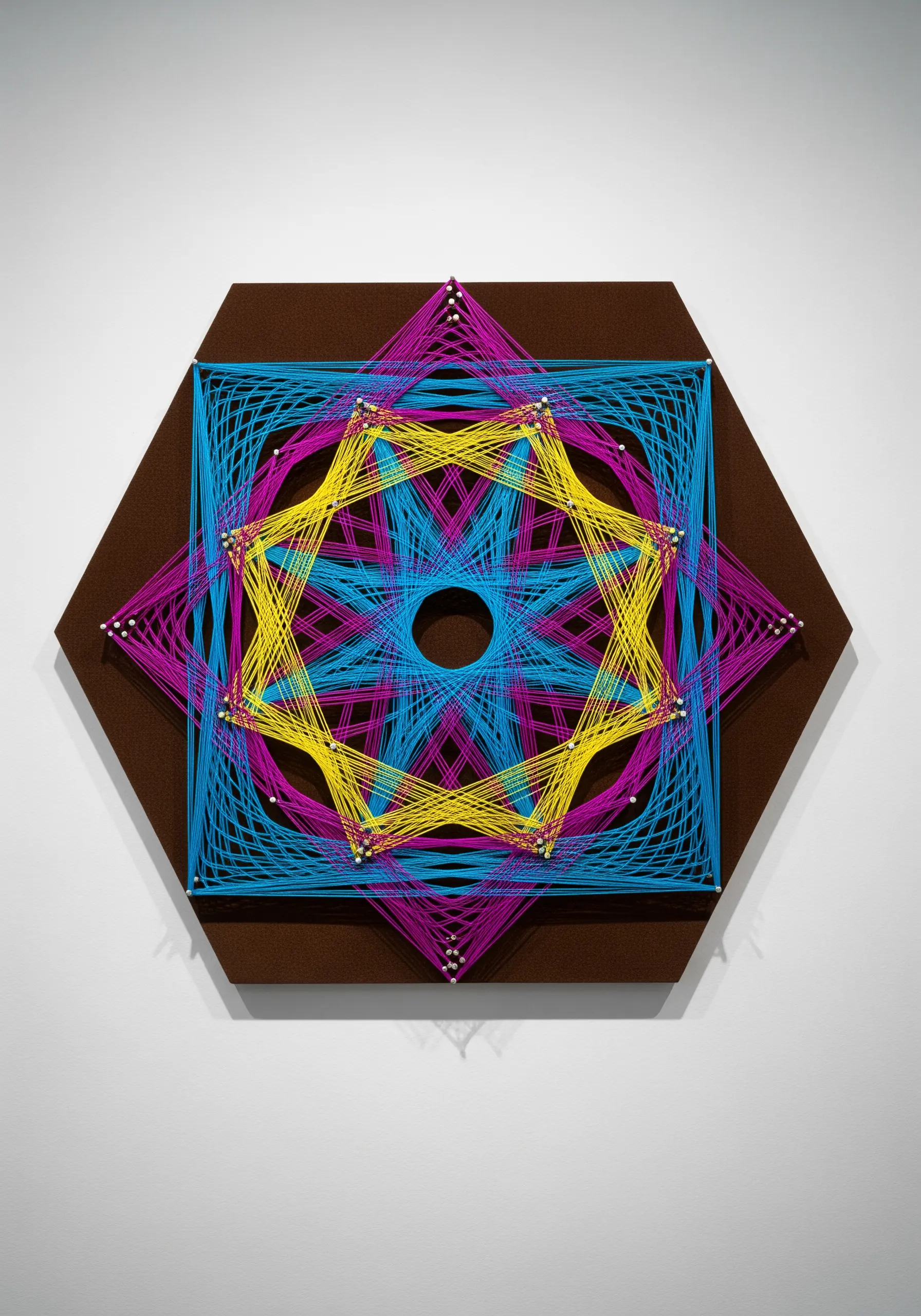 Hexagonal string art with overlapping geometric shapes in cyan, magenta, and yellow