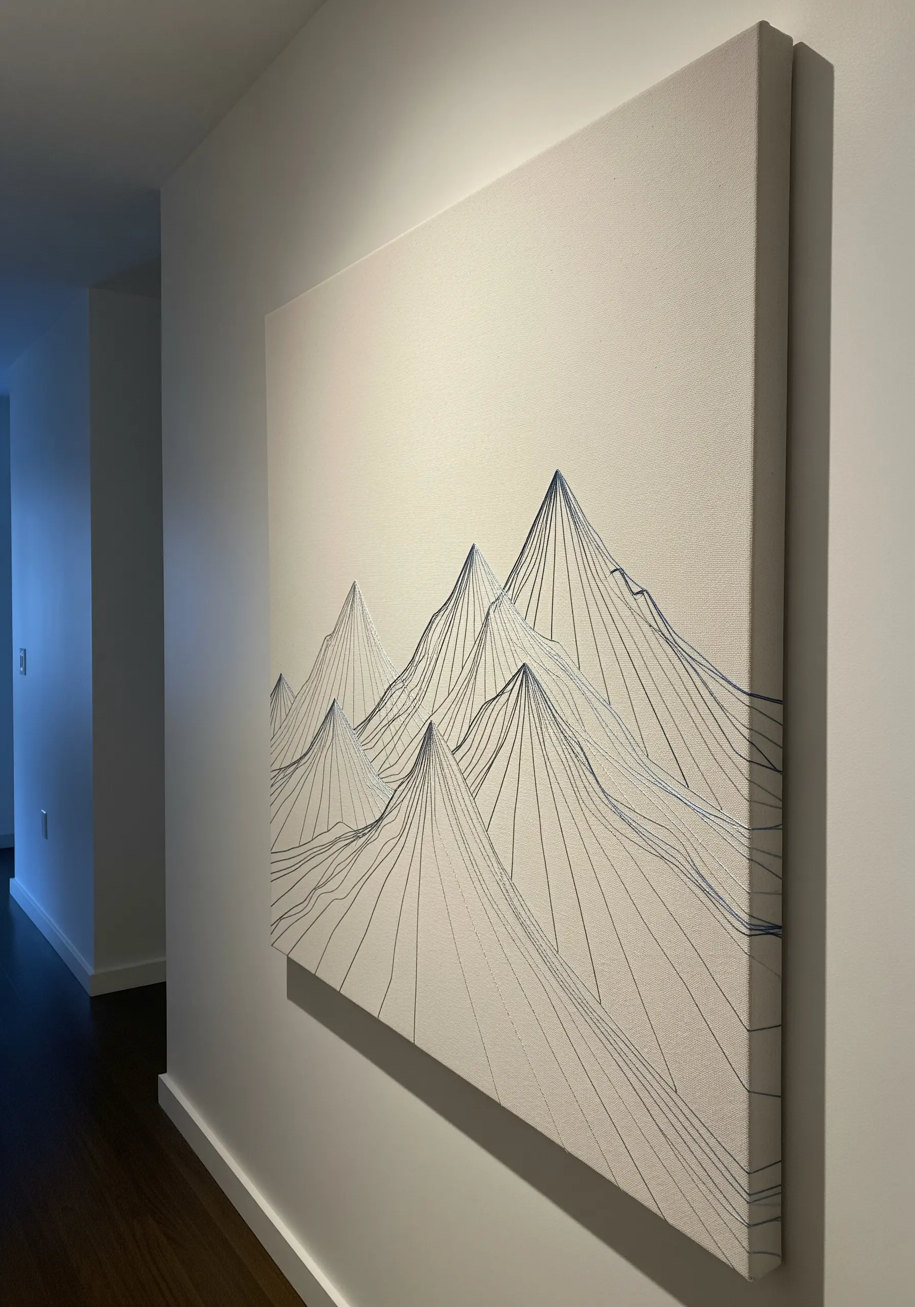 A large canvas with an abstract mountain range created with layered black and blue straight stitches.