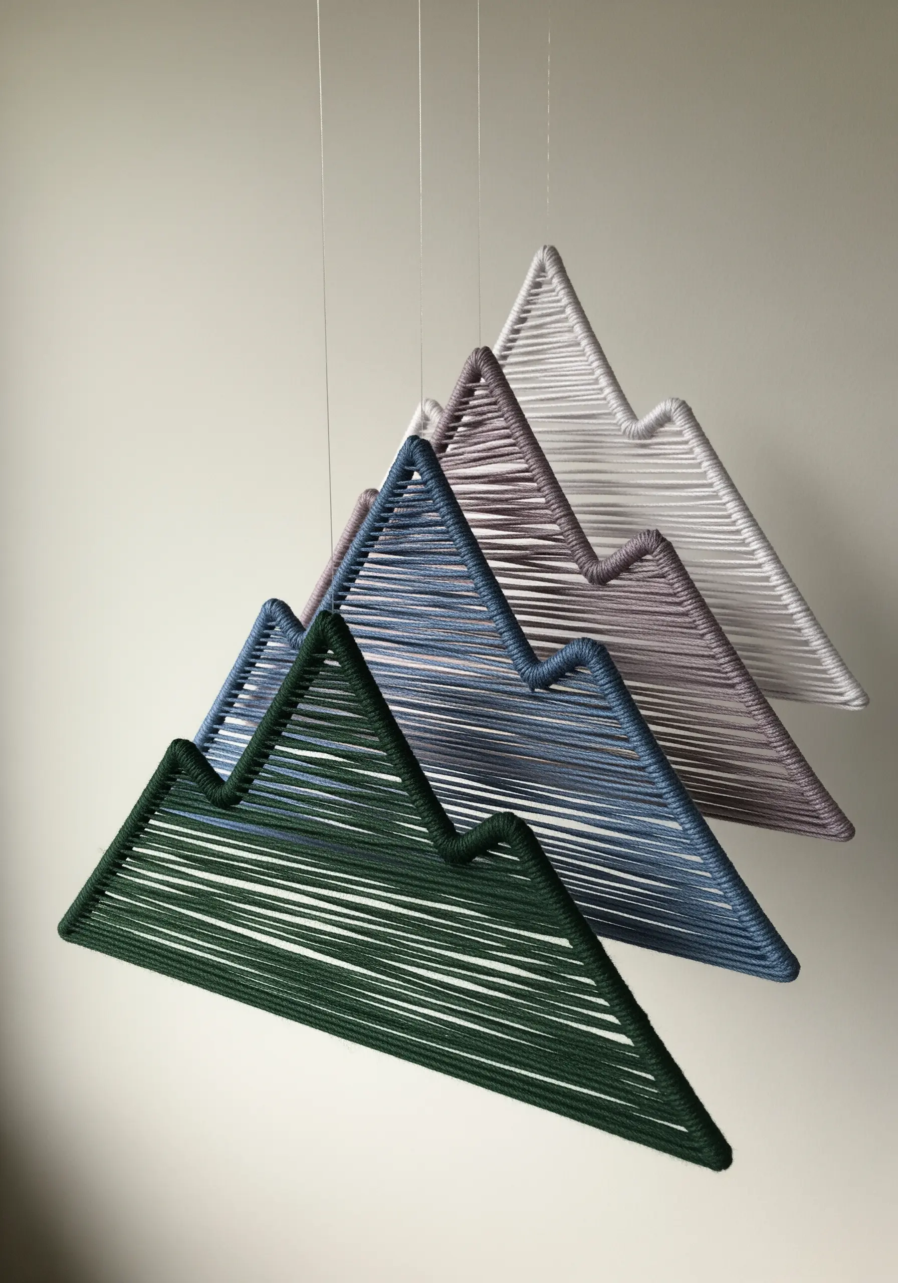 Four layered mountain-shaped wire frames wrapped in green, blue, mauve, and white thread.