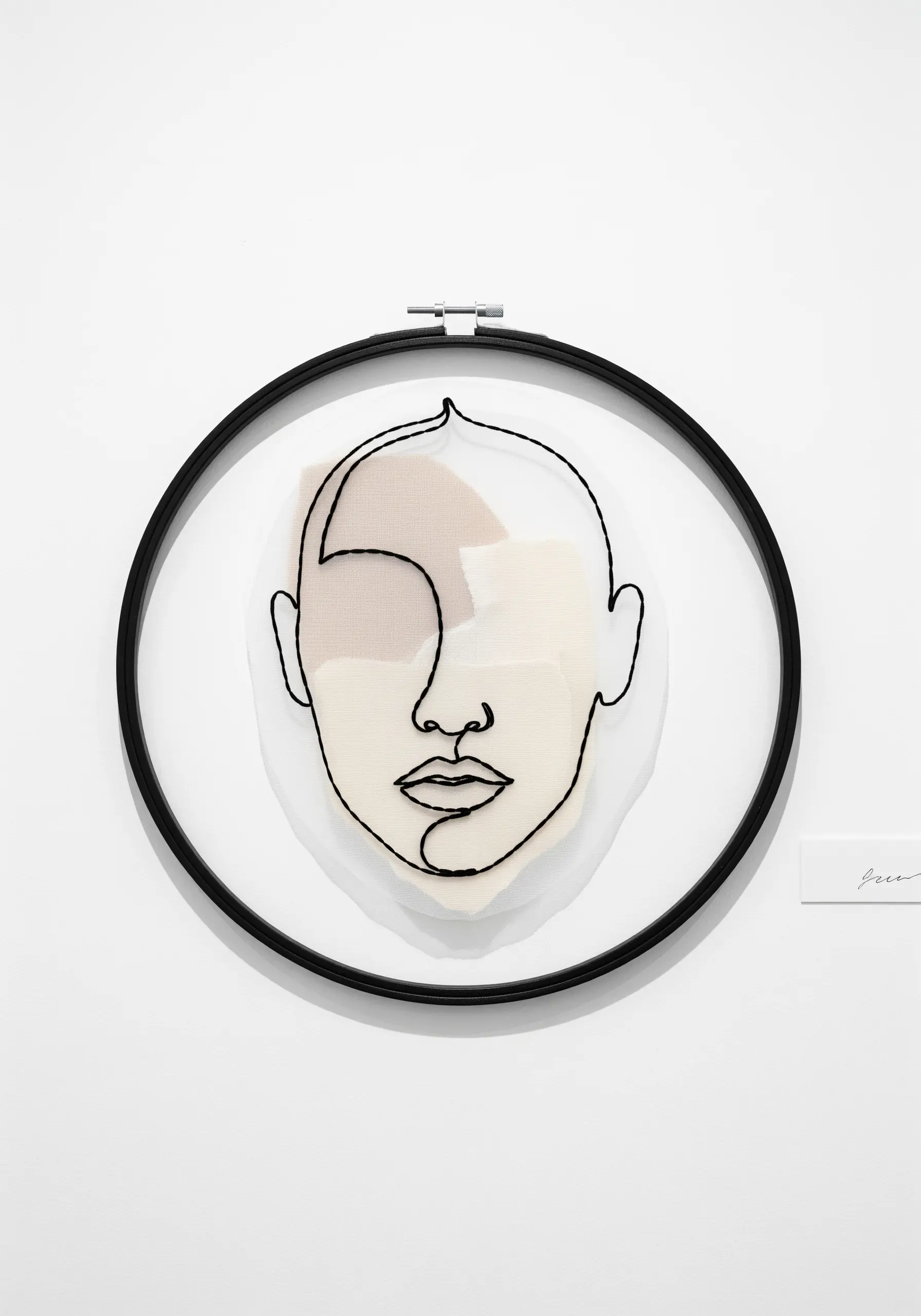 A single-line face portrait made with couched thread over sheer, layered fabric collage.