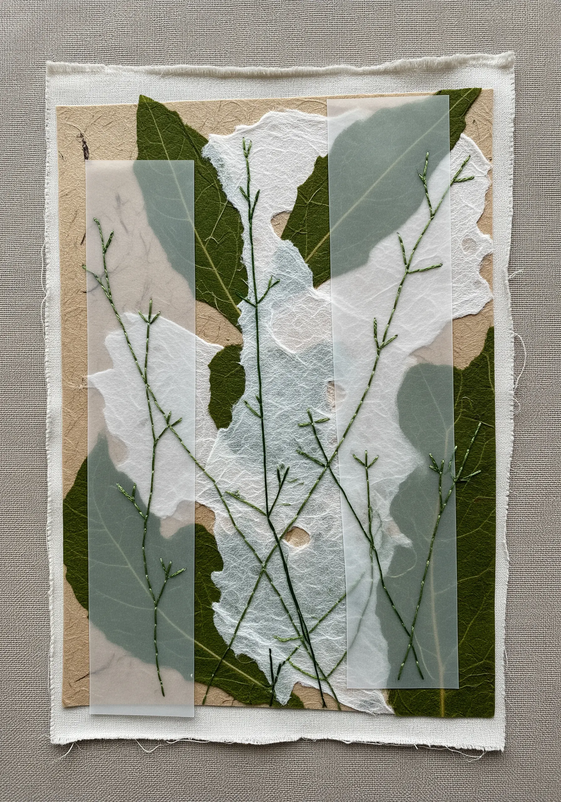 A collage of handmade paper, leaves, and vellum, with delicate green stems stitched across.