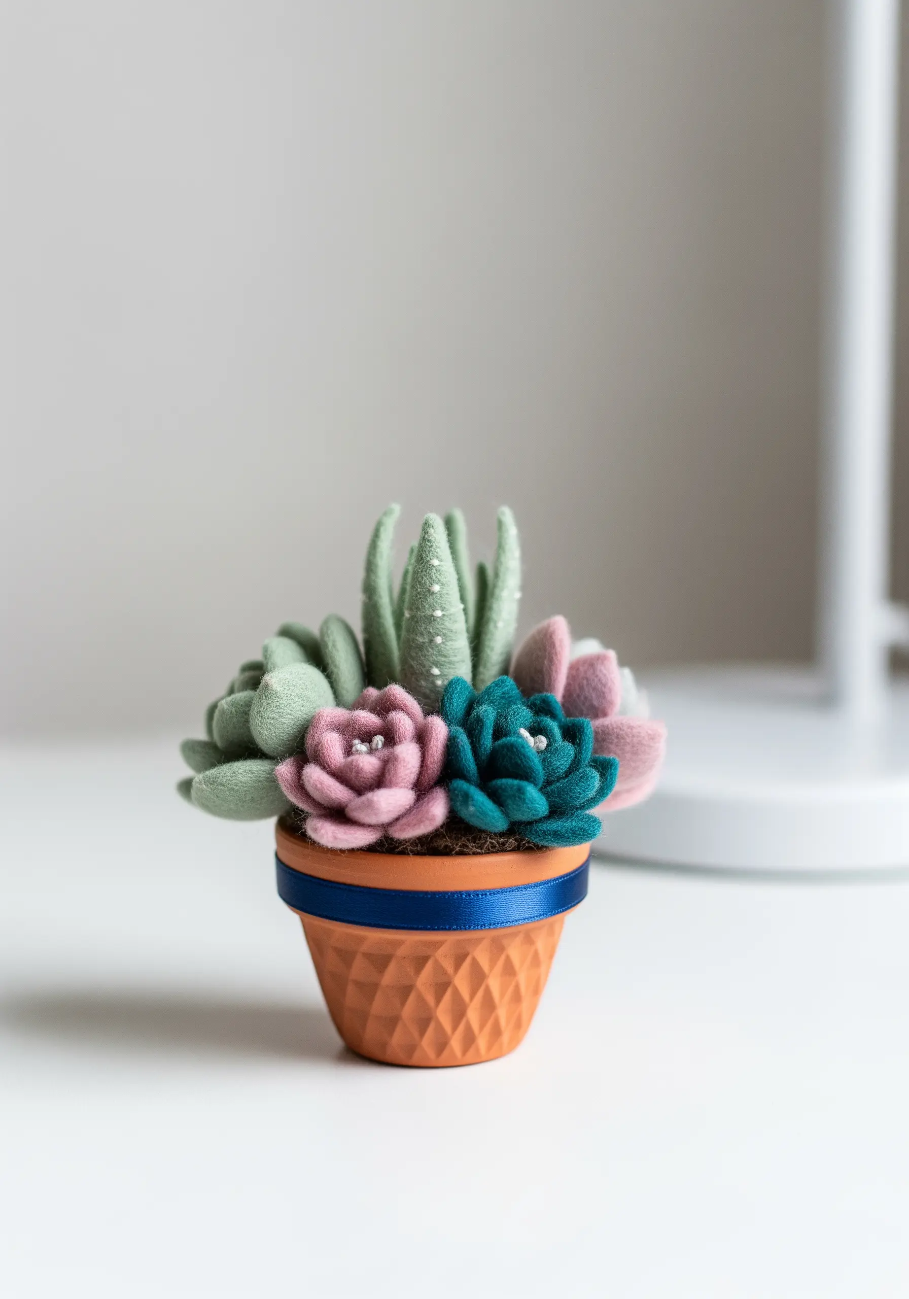 A small terracotta pot filled with handmade felt succulents in green and pink.