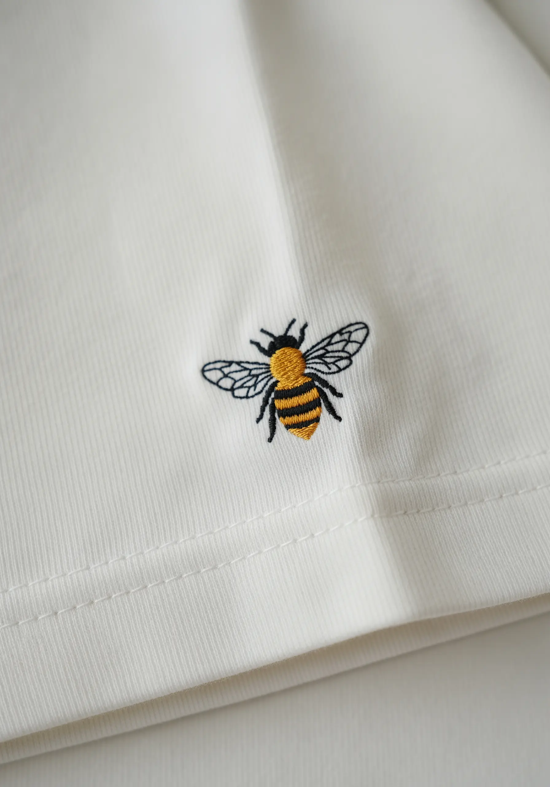 A detailed embroidered bee with textured yellow and black stripes on a white t-shirt.