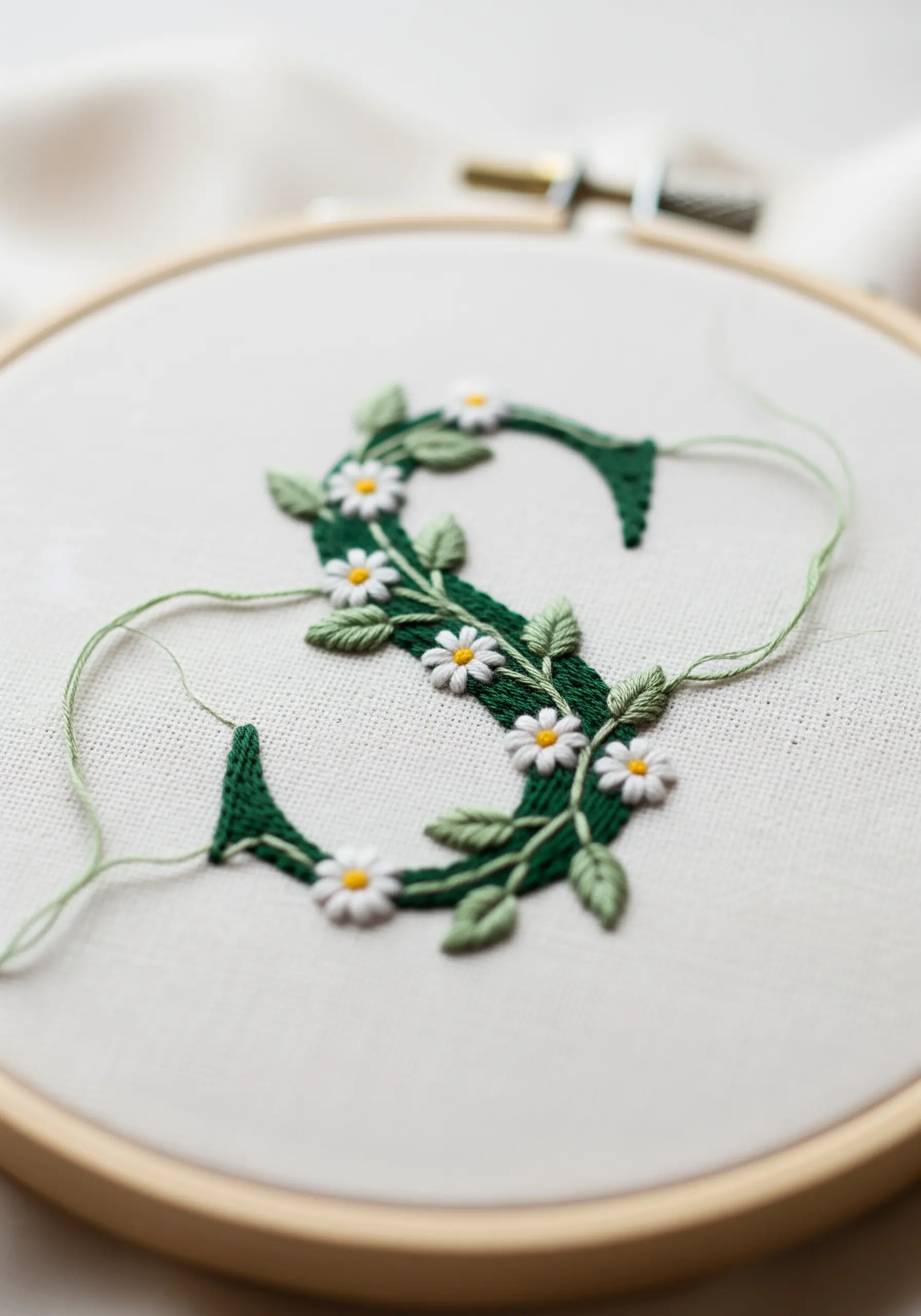 Floral monogram 'S' with embroidered white daisies and twining green leaves.