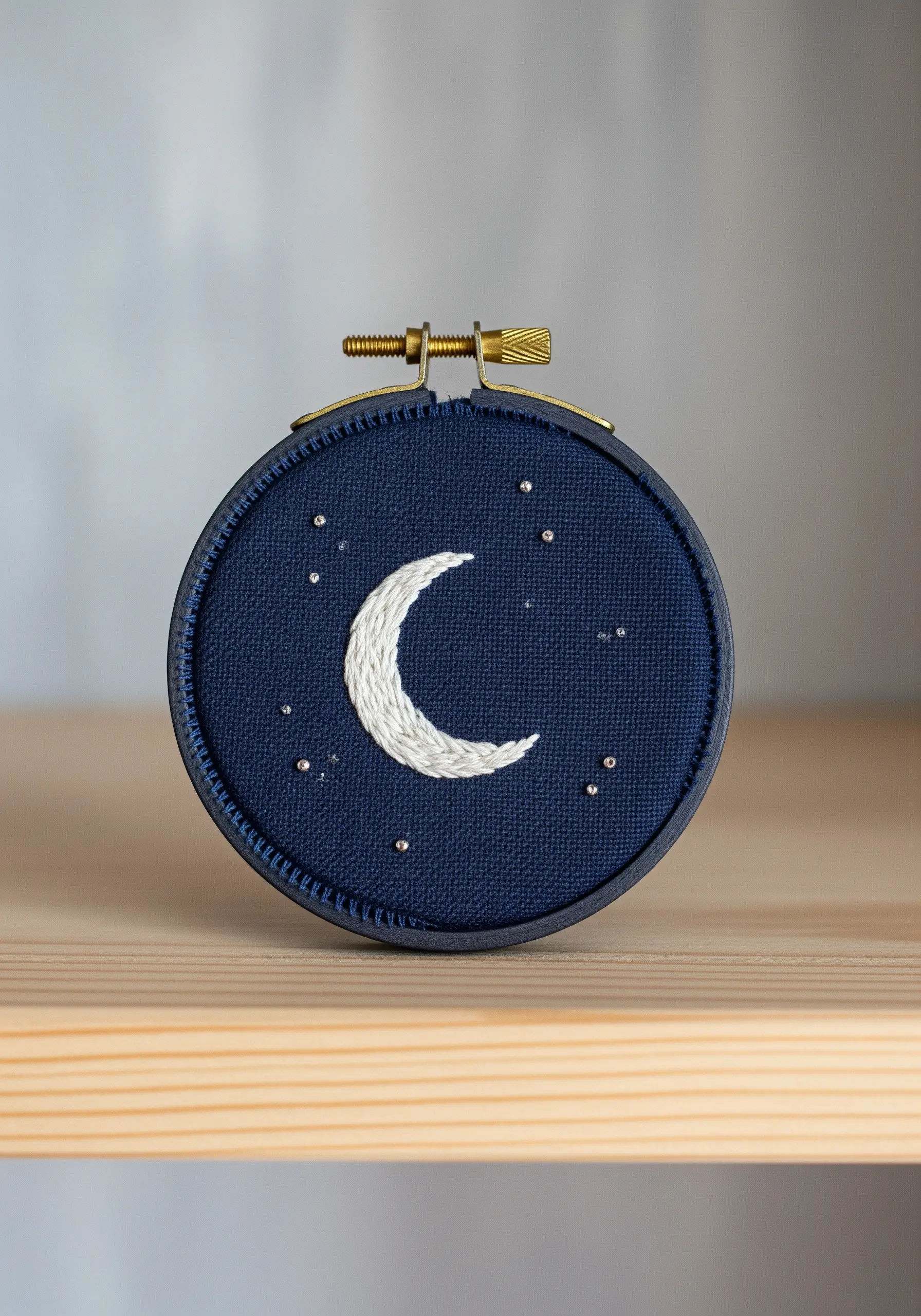 White crescent moon embroidered on dark blue fabric with tiny star stitches.