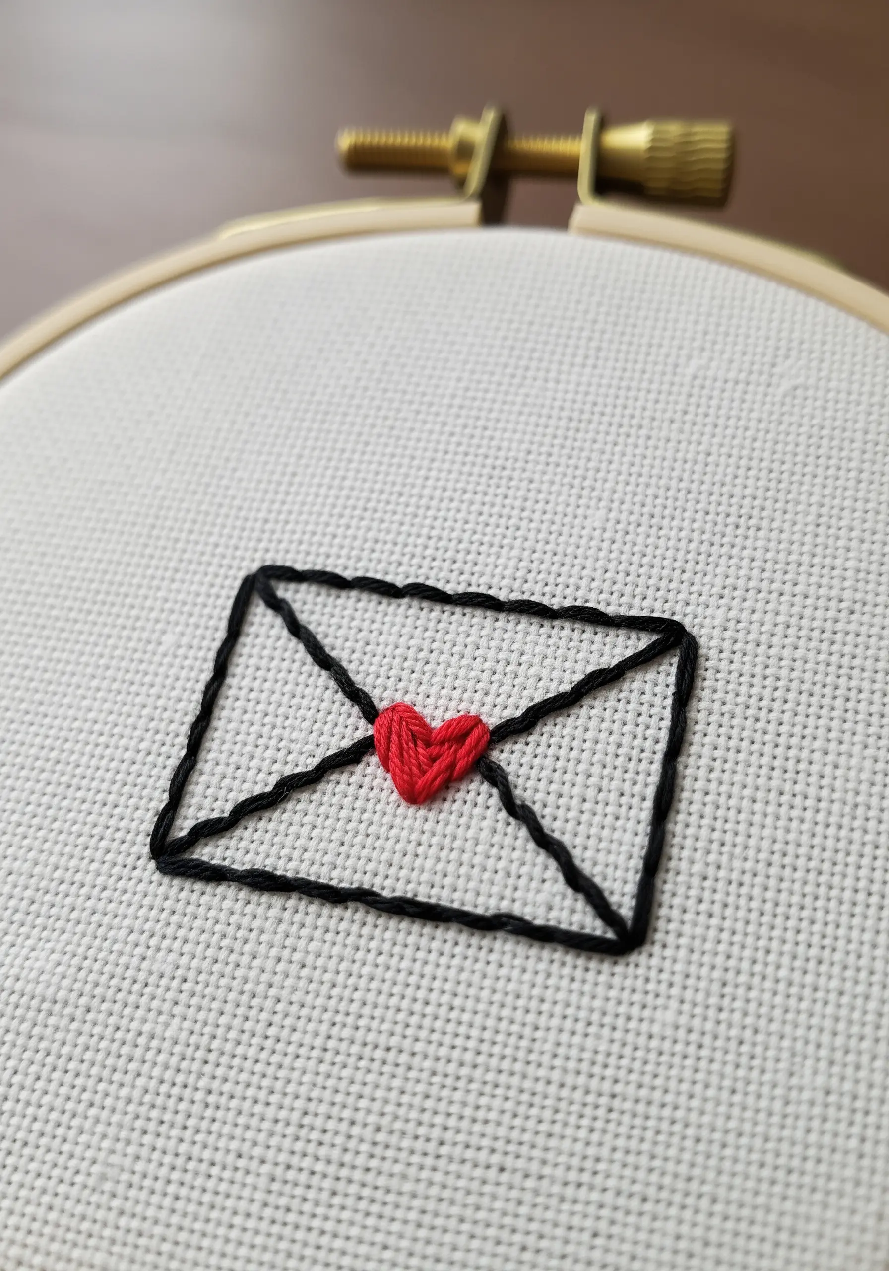 A minimal black outline of an envelope with a raised, red satin stitch heart in the center.