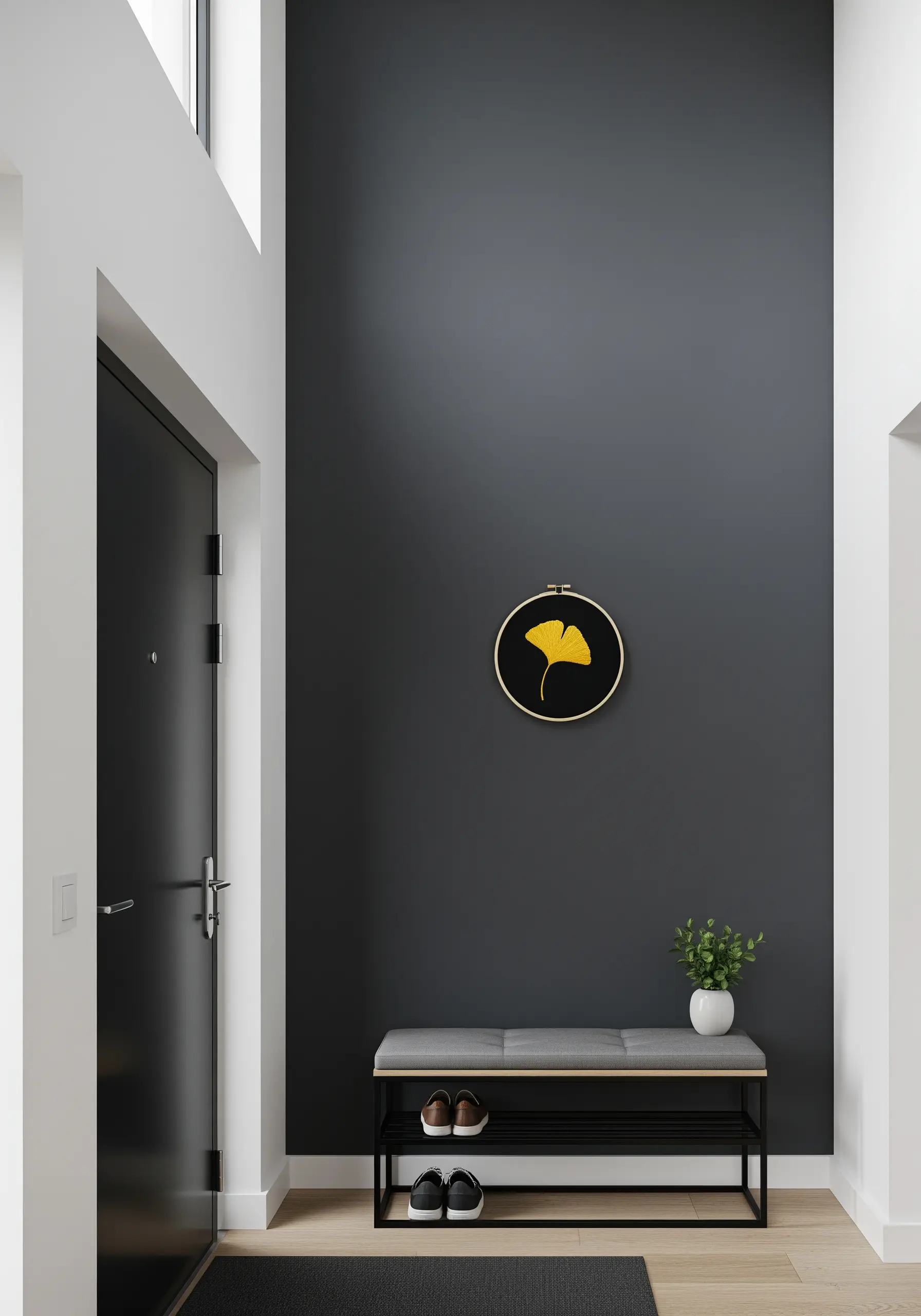 A single, bright yellow embroidered ginkgo leaf in a hoop on a dark gray wall.