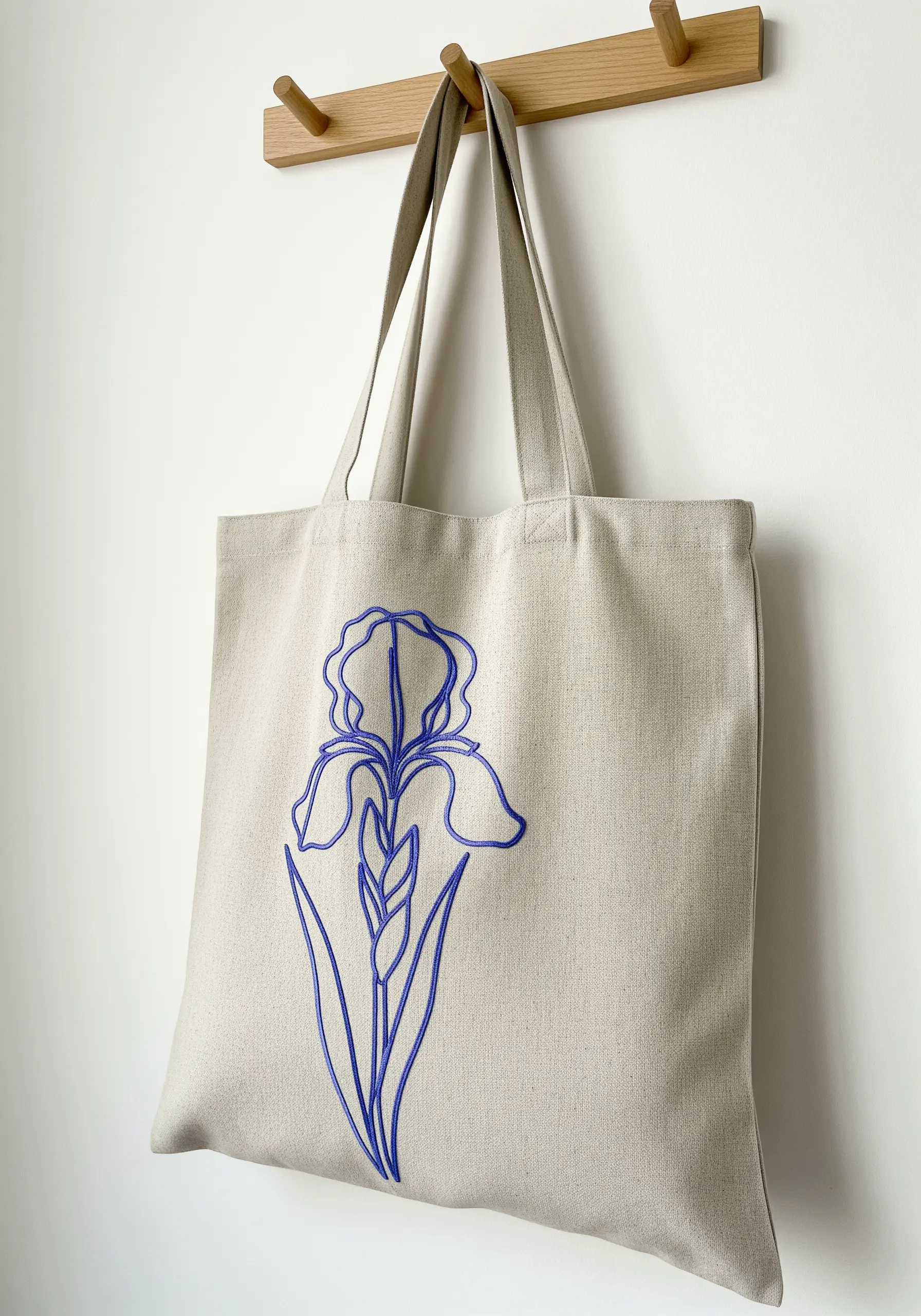 Minimalist line art embroidery of an iris flower in bold blue thread on a canvas tote bag.