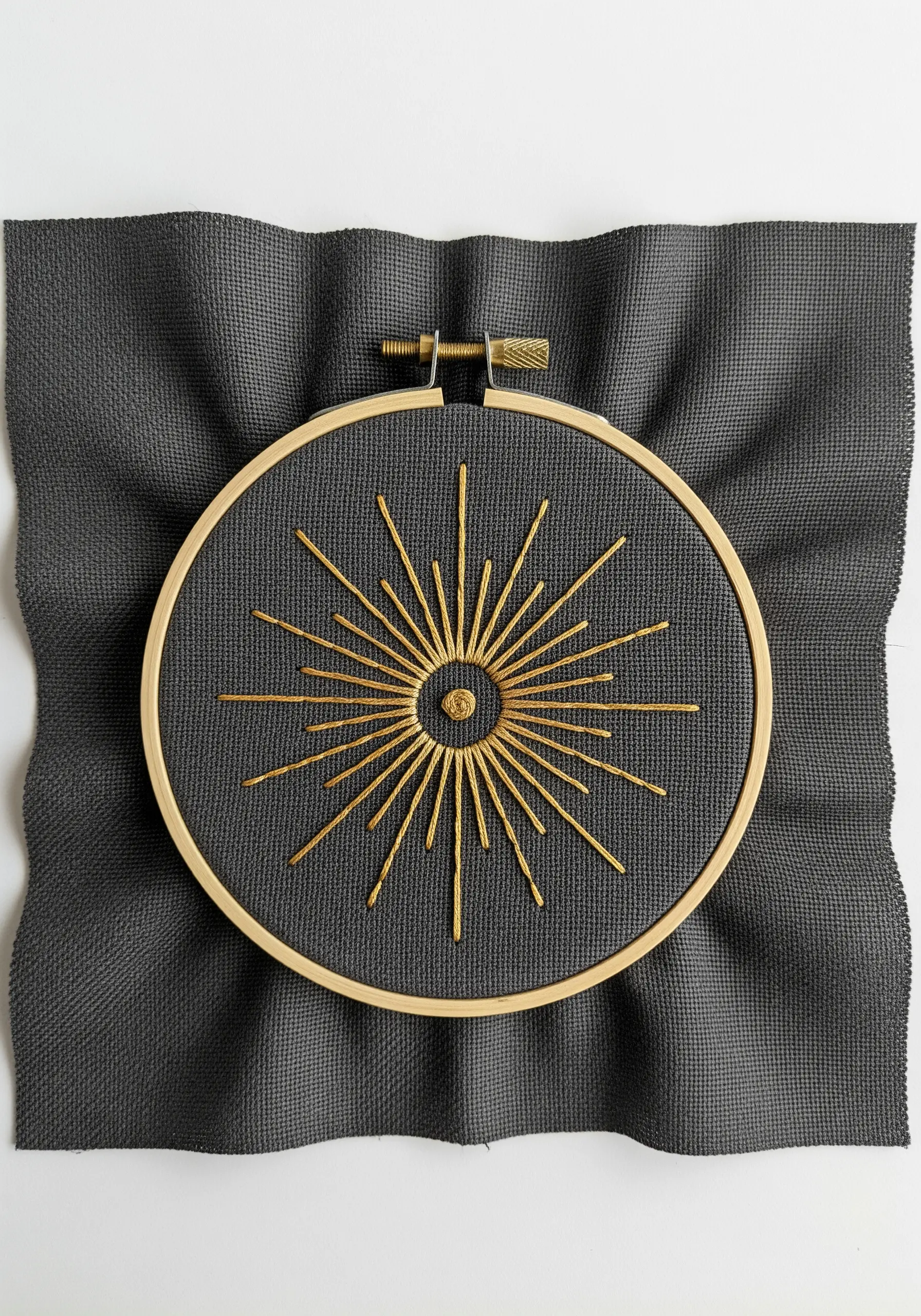 A sunburst with metallic gold rays embroidered on a dark charcoal grey fabric.