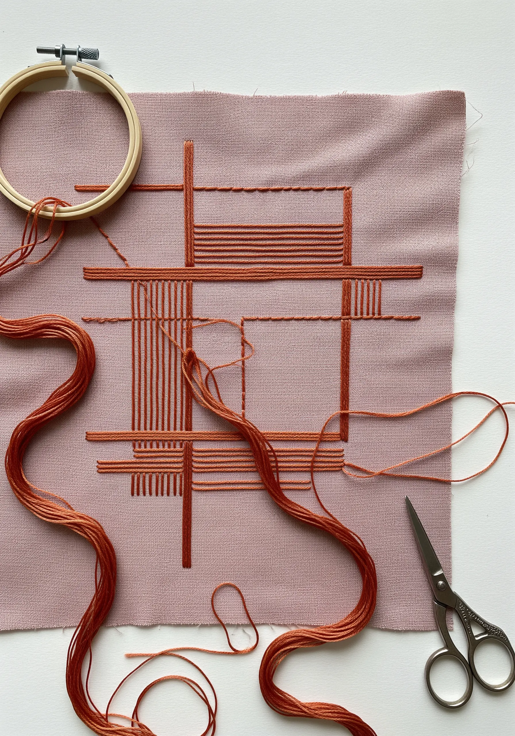 An in-progress architectural embroidery in terracotta thread on dusty rose fabric.