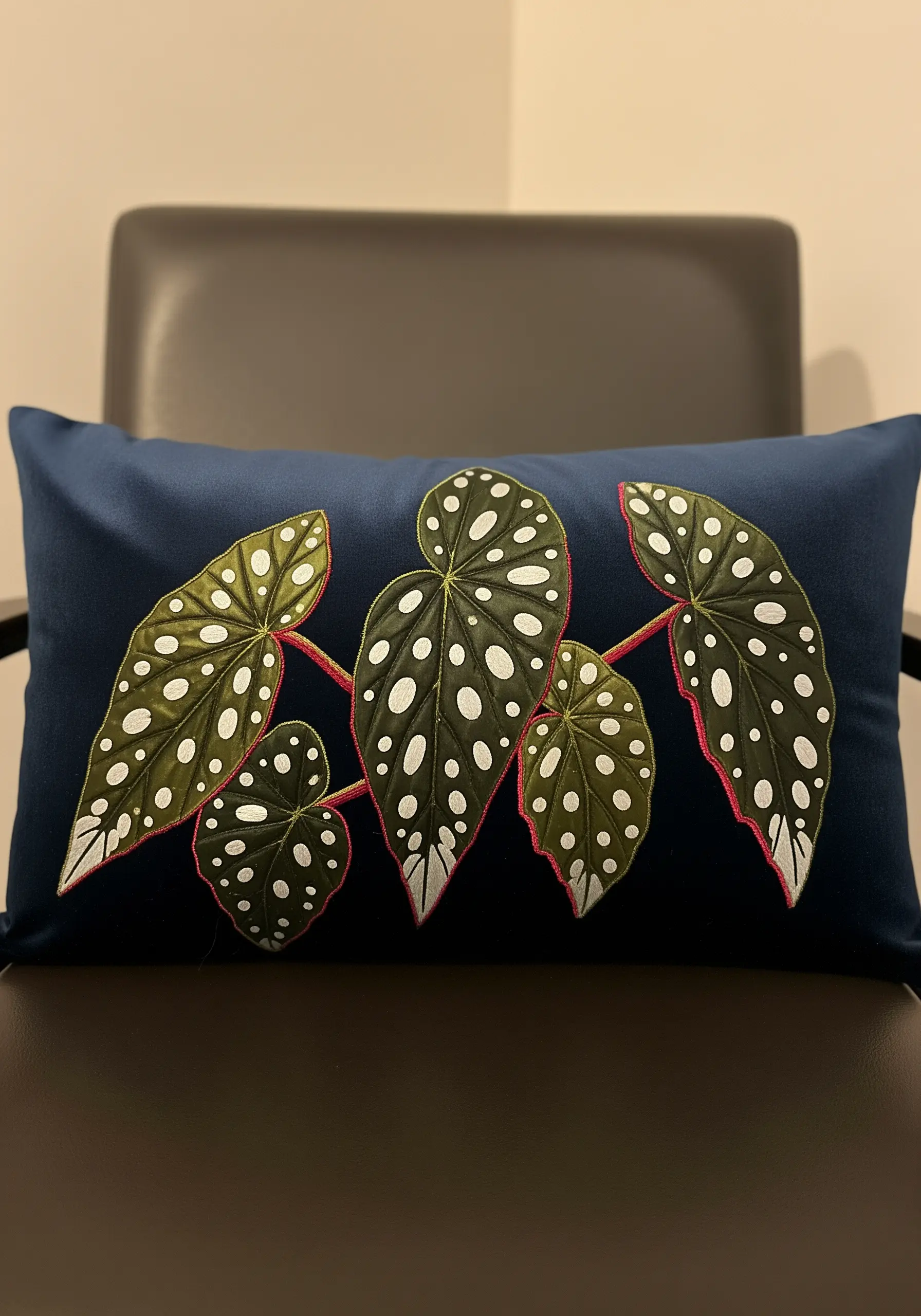 Appliqué and embroidered Begonia leaves with white French knot spots on a navy blue pillow.