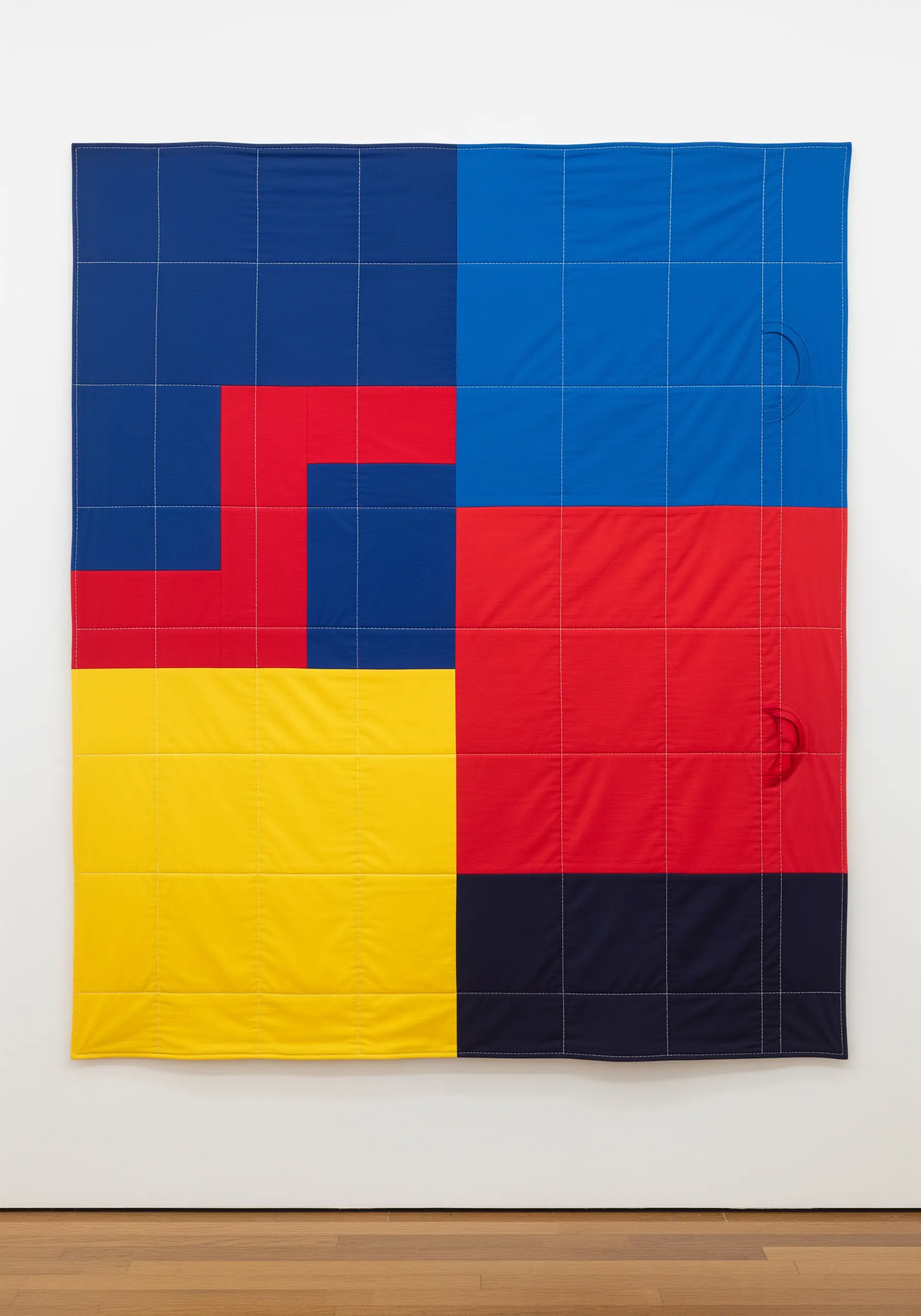 A modern, color-blocked quilt in red, yellow, and blue with a white stitched grid.