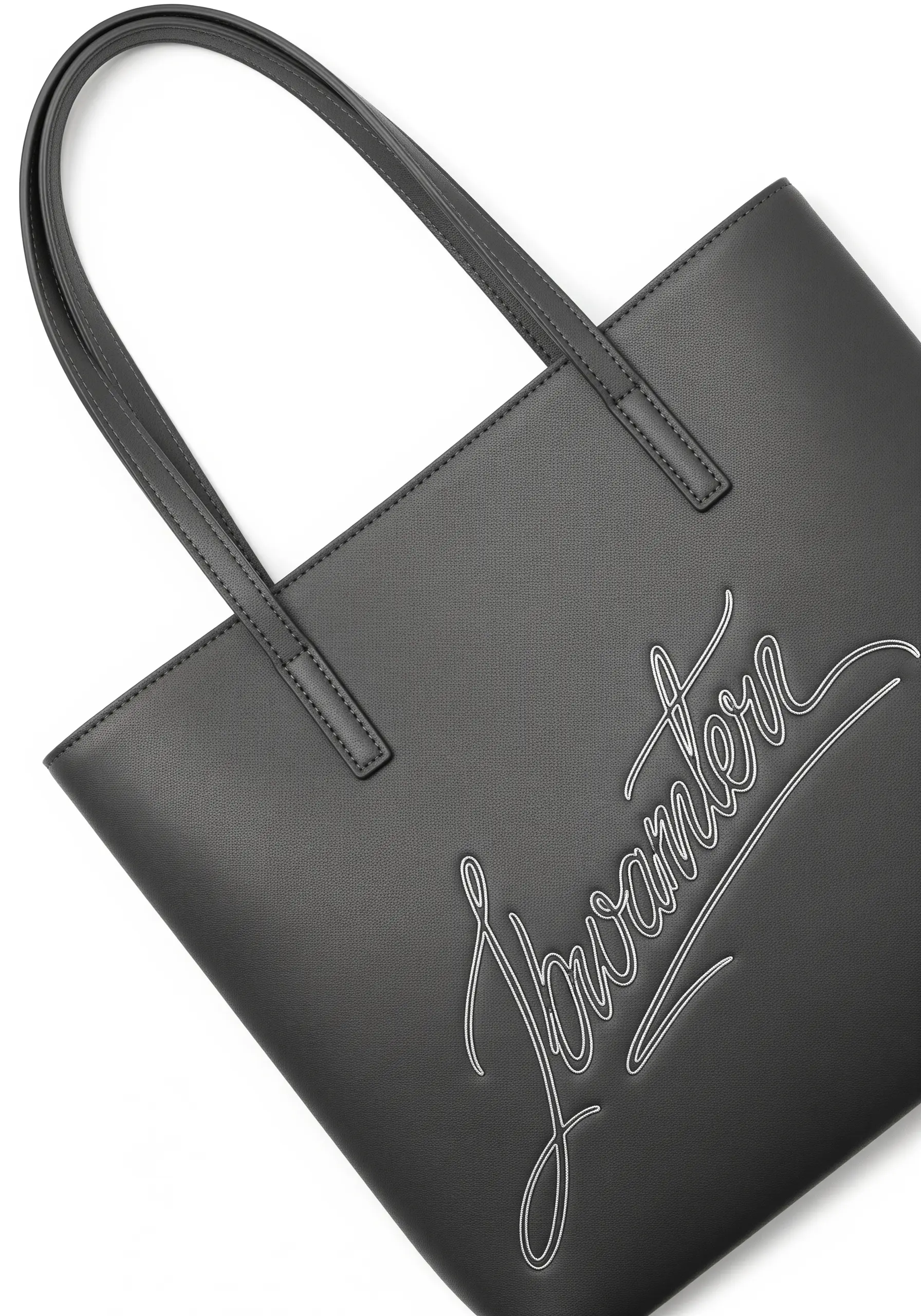 Delicate white script signature embroidered onto a black faux leather tote bag.