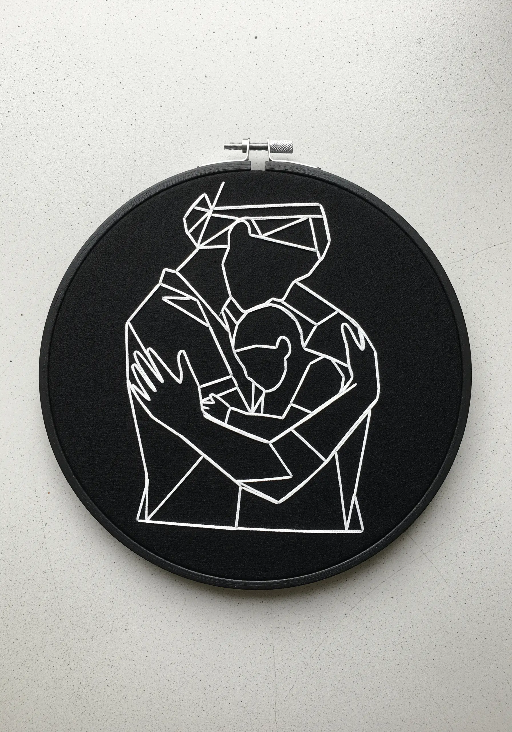 A geometric, faceted line art design of two figures hugging, stitched in white on black fabric.