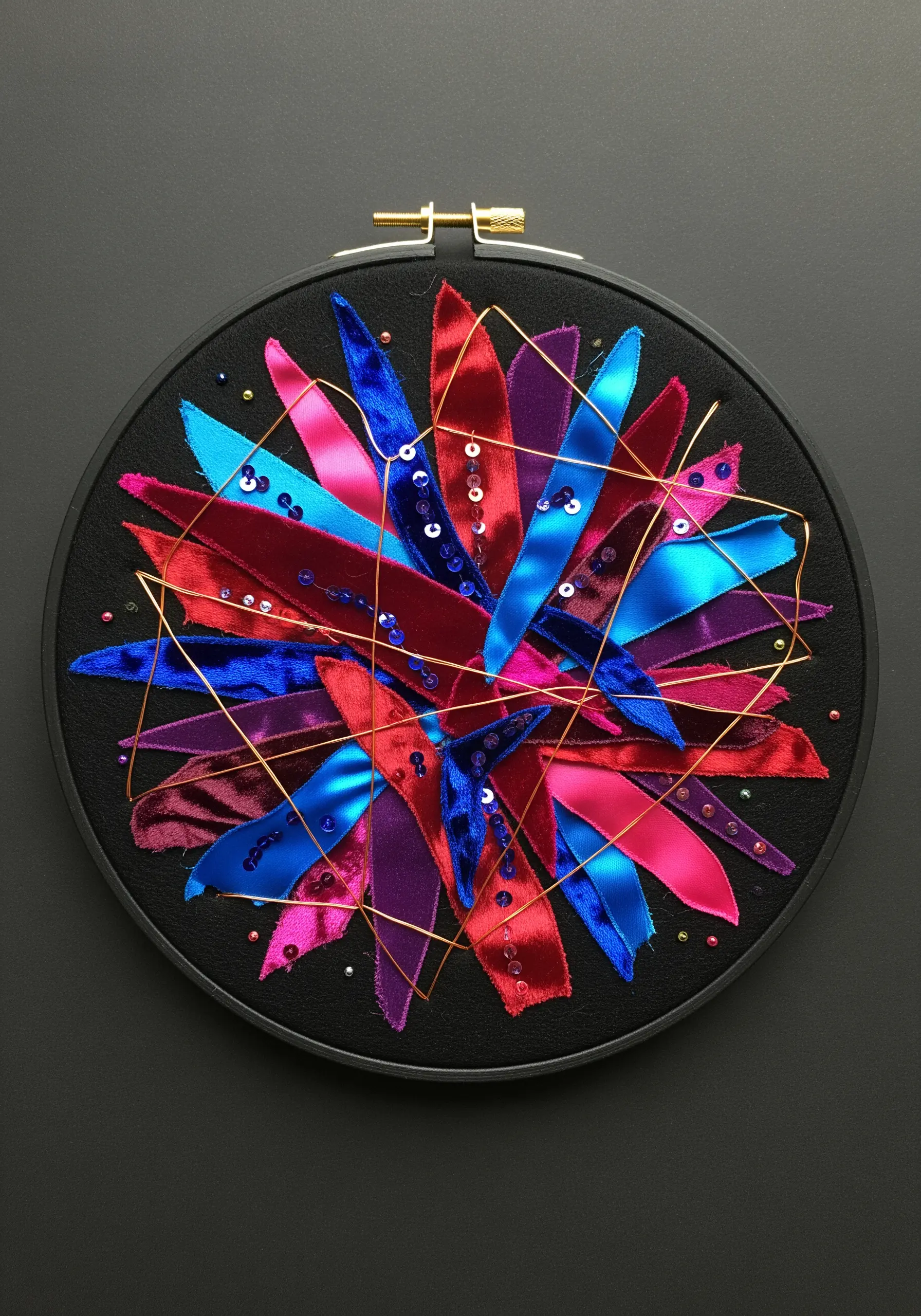 Abstract starburst made from layered satin and velvet ribbons with metallic thread and sequins.