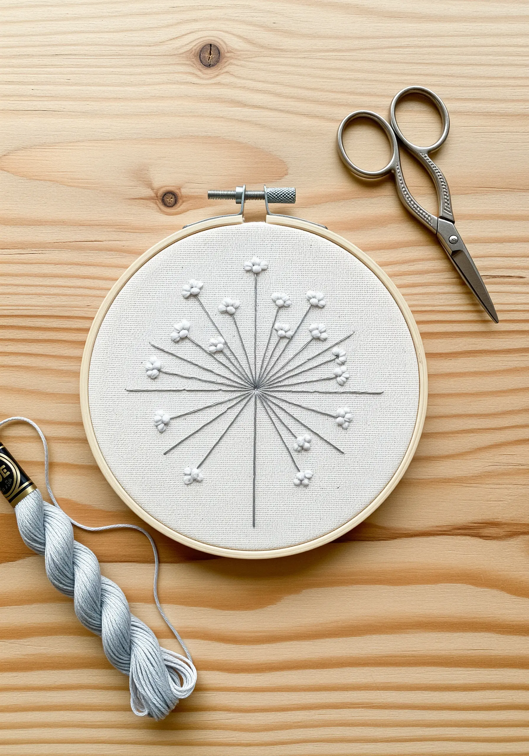 Minimalist grey floral embroidery on white fabric, using French knots and straight stitches.