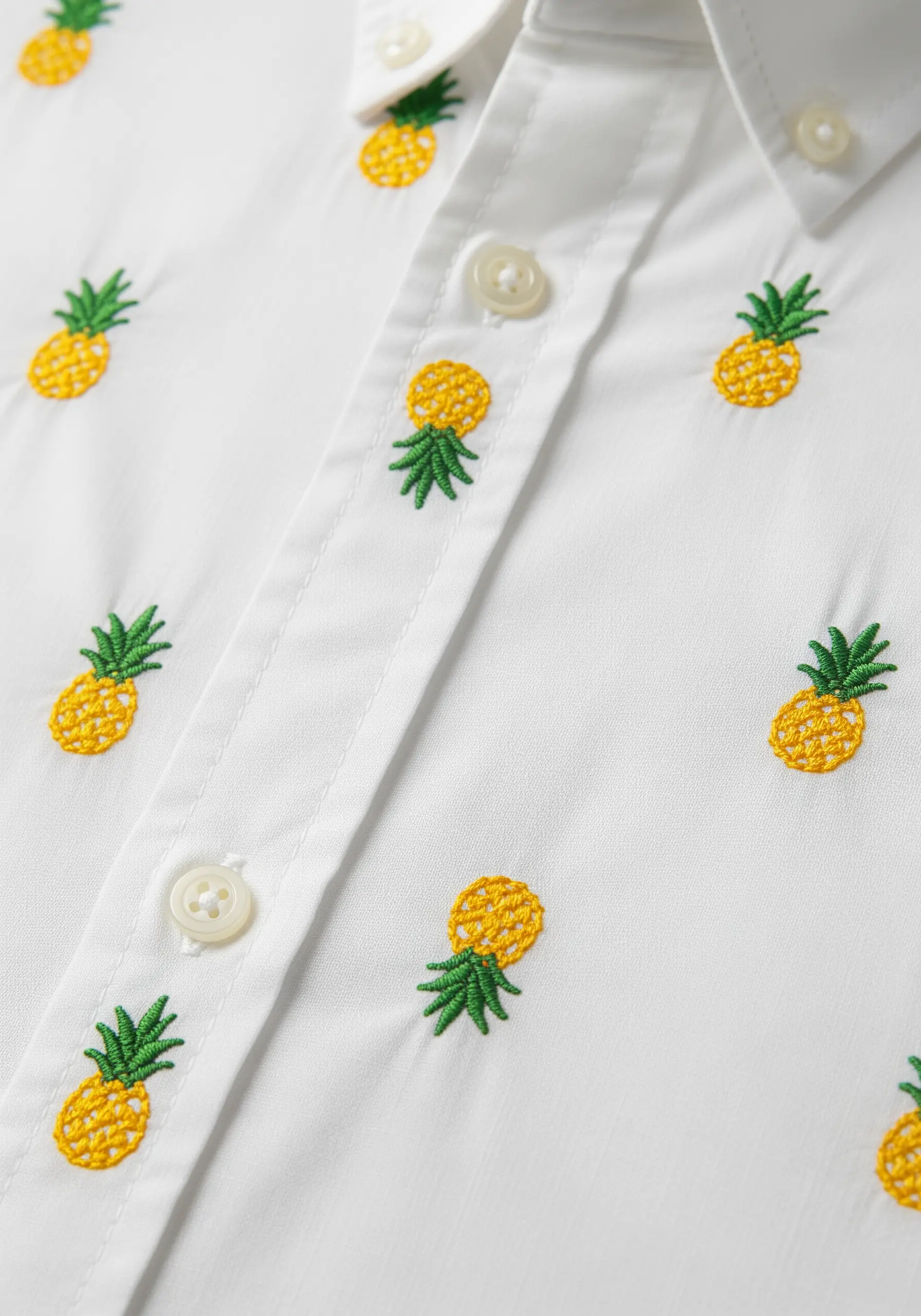 Small embroidered pineapples arranged in a repeating pattern on a white button-down shirt.