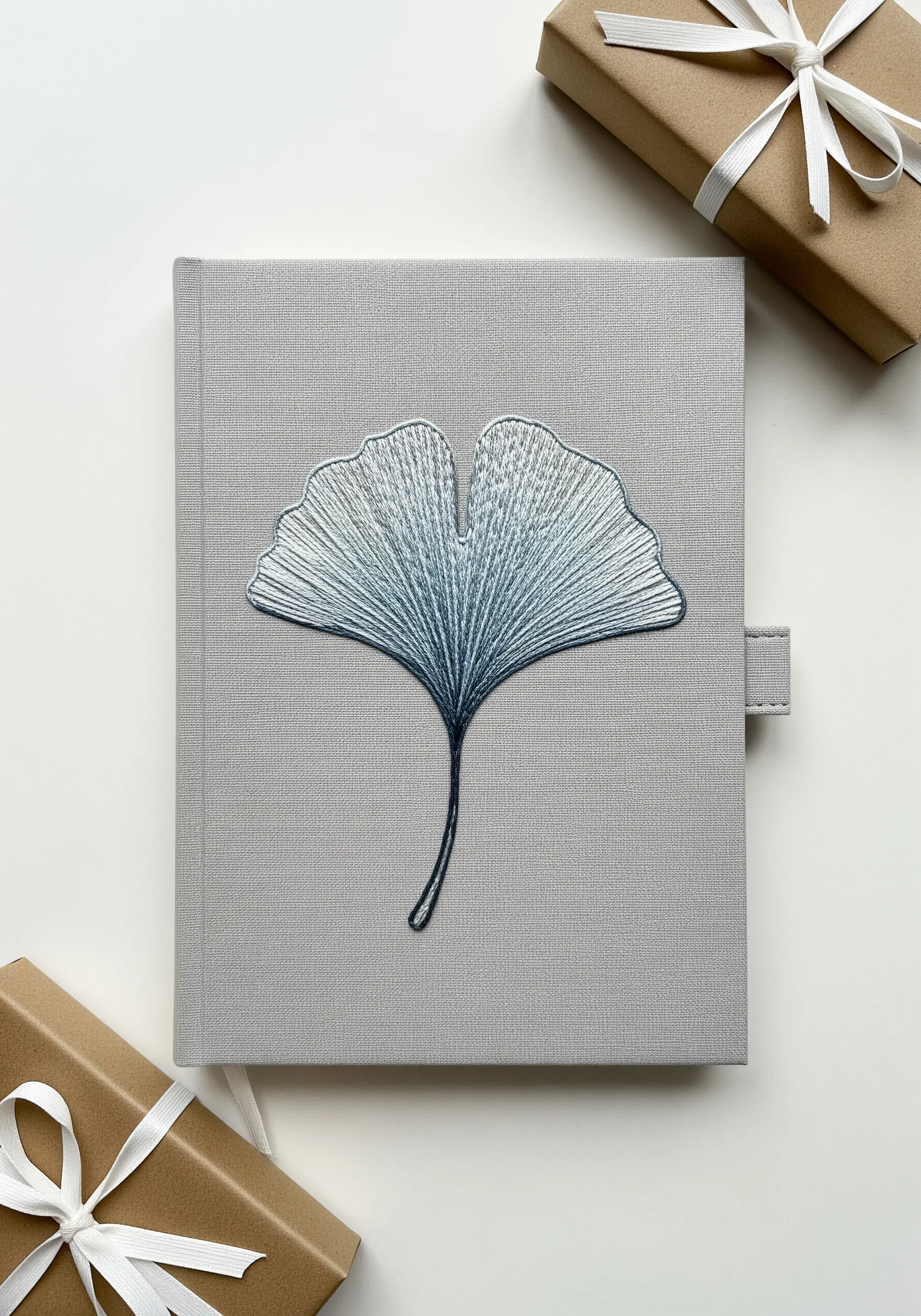 A blue-grey ginkgo leaf embroidered with radiating satin stitch on a journal cover.