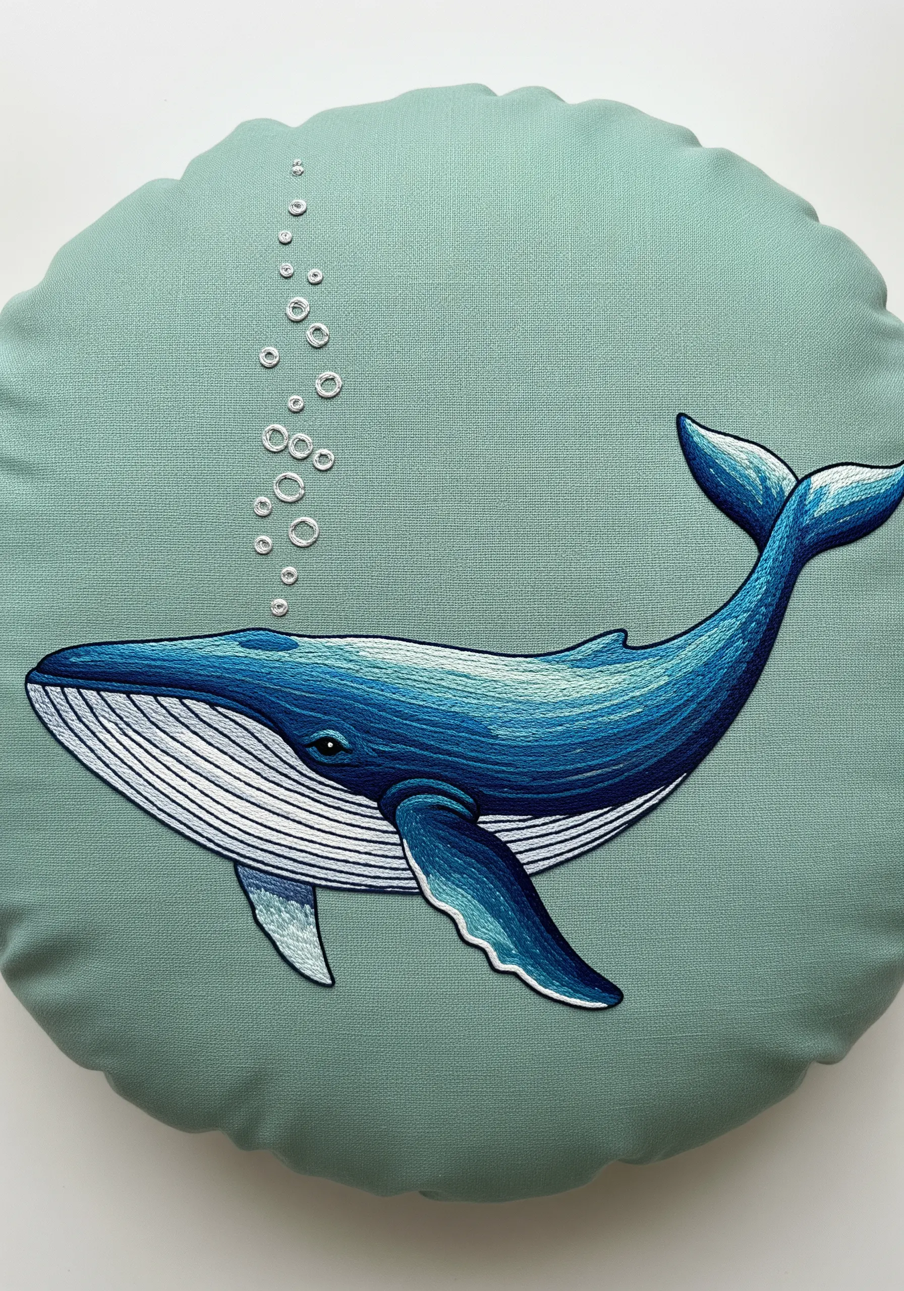 Thread-painted whale on a green pillow with smooth blue color gradients.