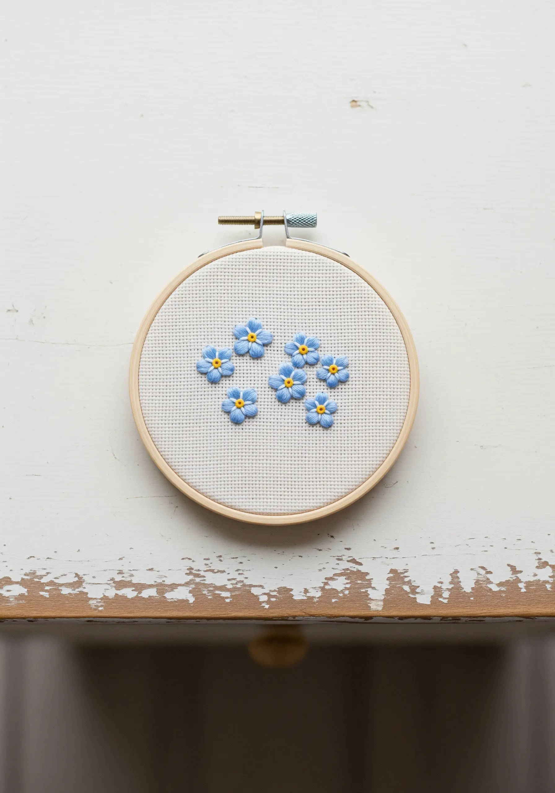 Scattered blue forget-me-not flowers with yellow centers stitched on gridded fabric in a hoop.
