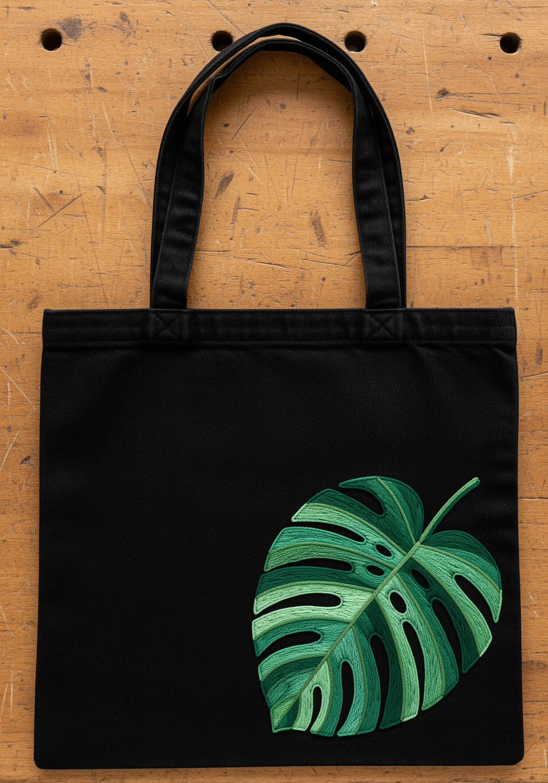A realistic, thread-painted monstera leaf with color gradients on a black tote bag.