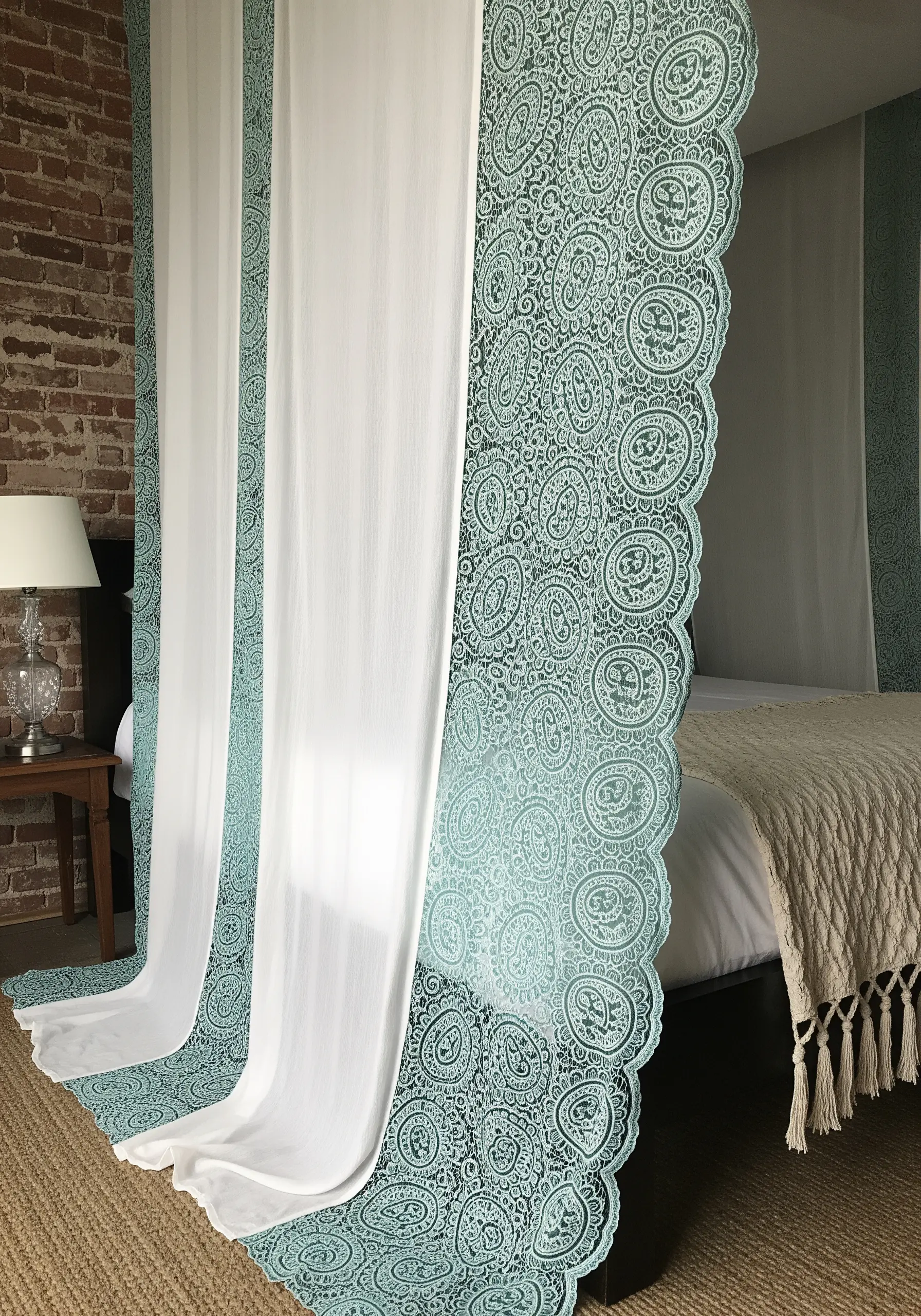 Sheer white bed curtains with a wide, intricate paisley border embroidered in teal thread.